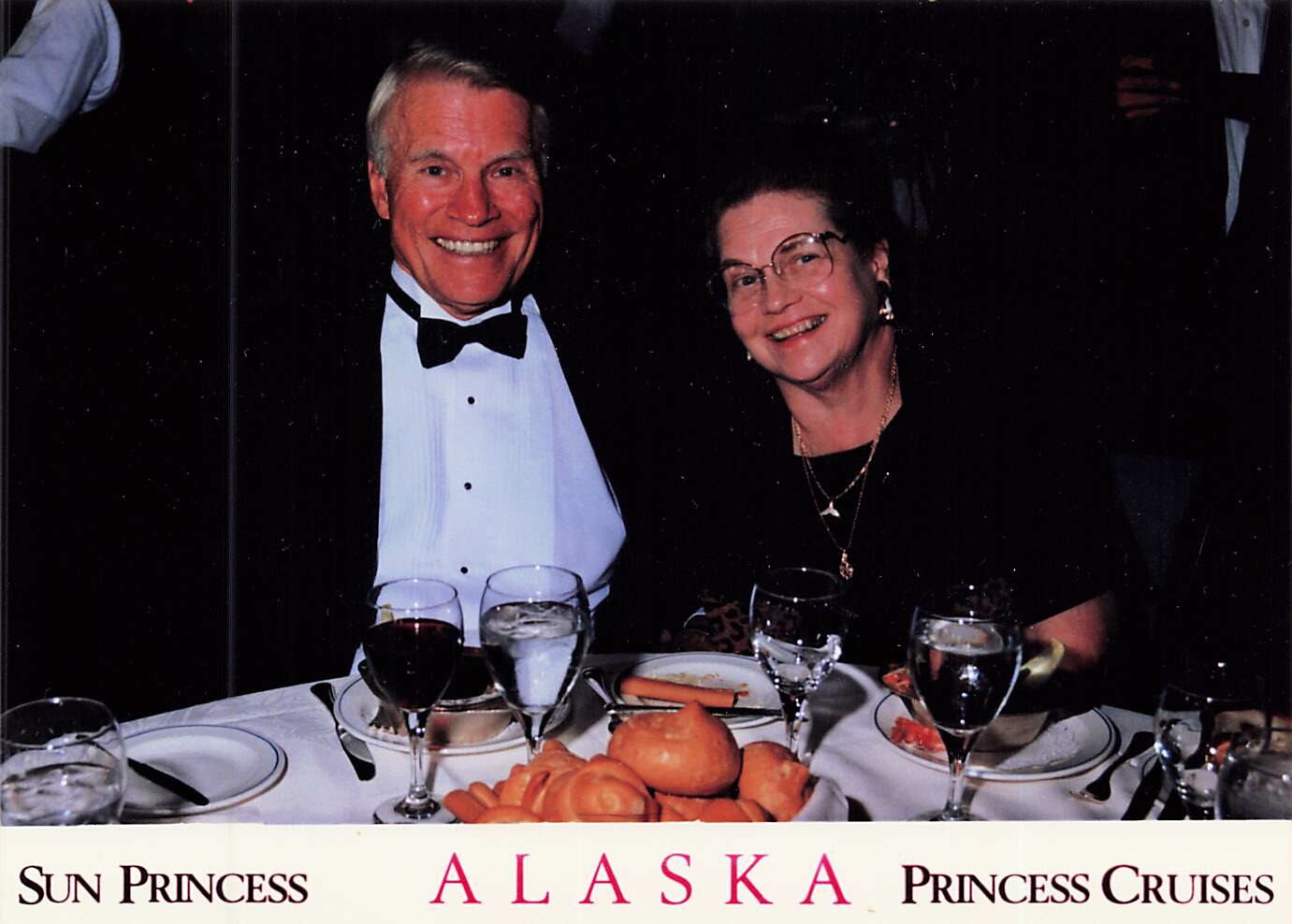 Smiling couple in formal wear at a Sun Princess Alaska Cruises dinner table on a ship cruise.]�INVALID