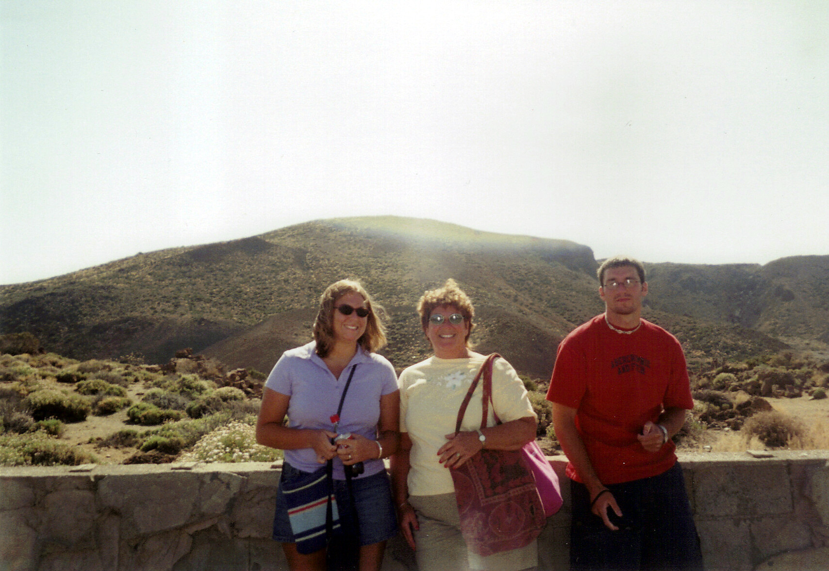 Three friends posing in a desert landscape with rocky hills in the background, smiling at the camera.