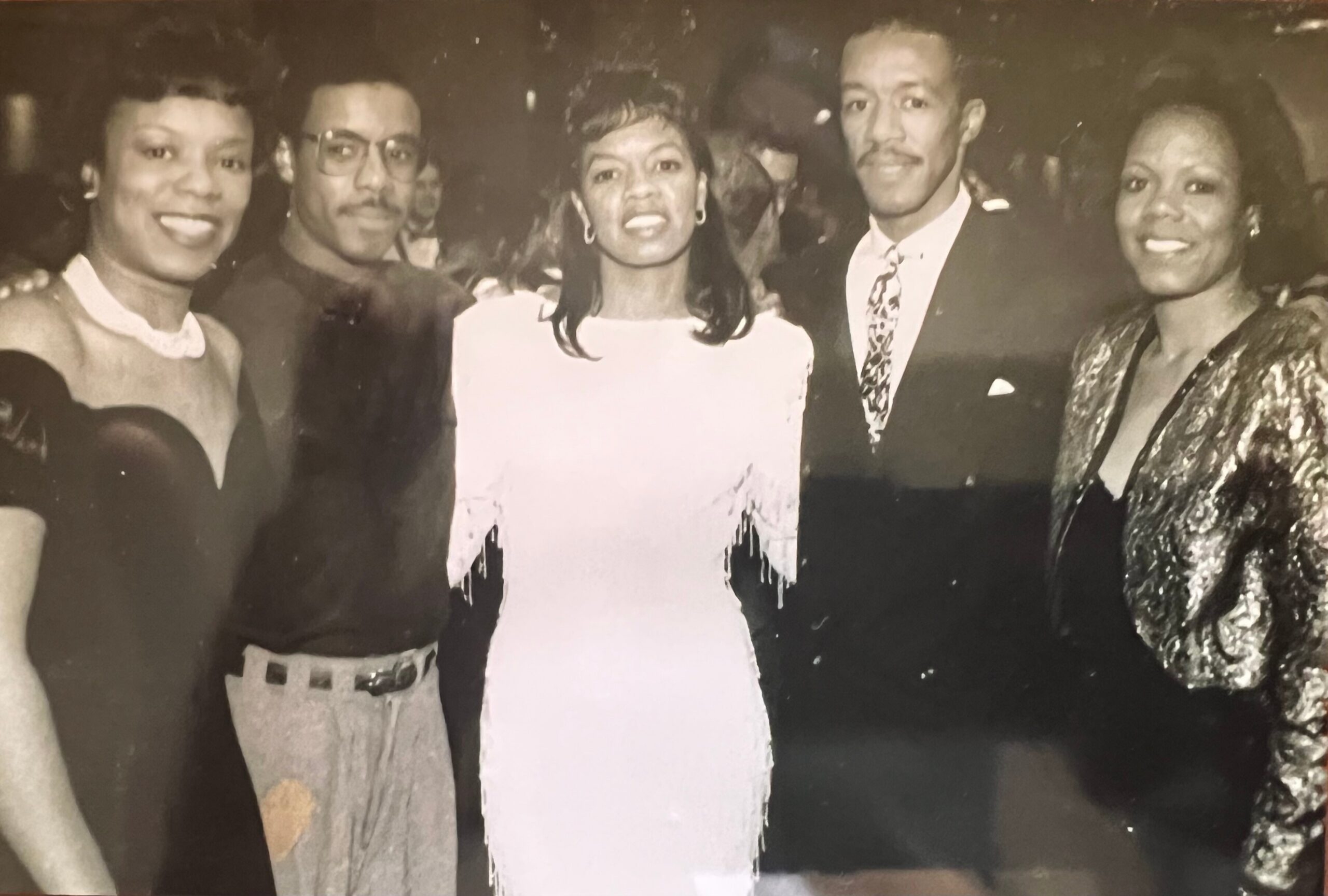Group of five people posing closely for a photo at a social event, all smiling at the camera.
