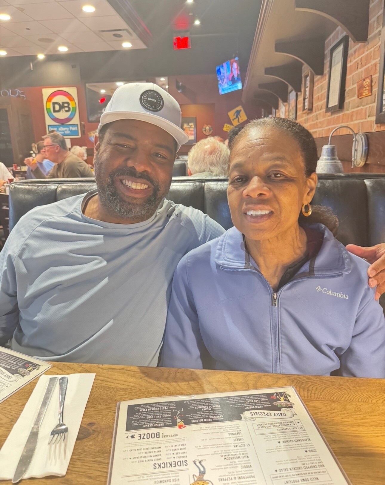 Smiling man and woman sit together in a booth at a restaurant, casual dining setting with menus on the table behind them.
