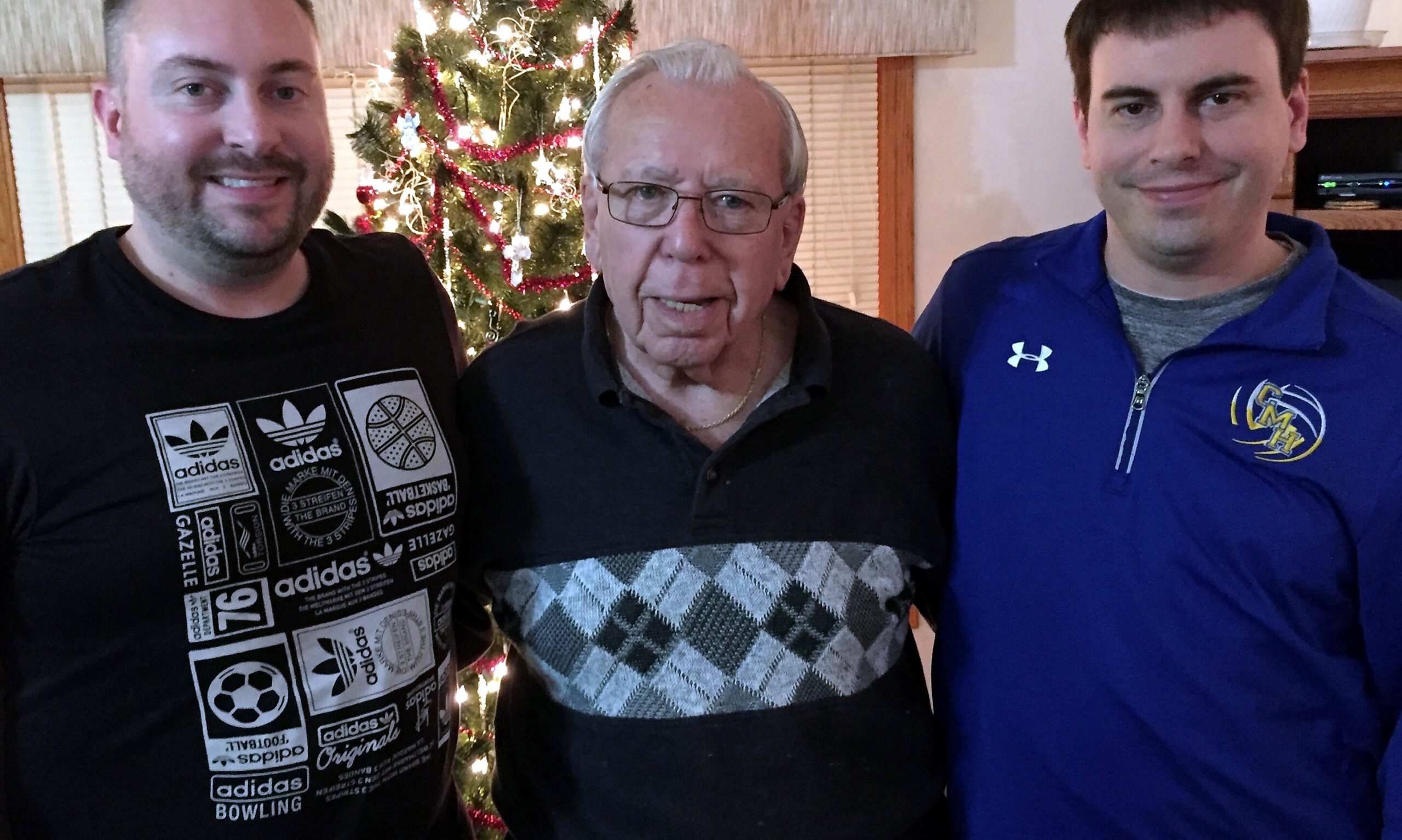 Three men posing for a photo indoors with a lit Christmas tree in the background behind them.