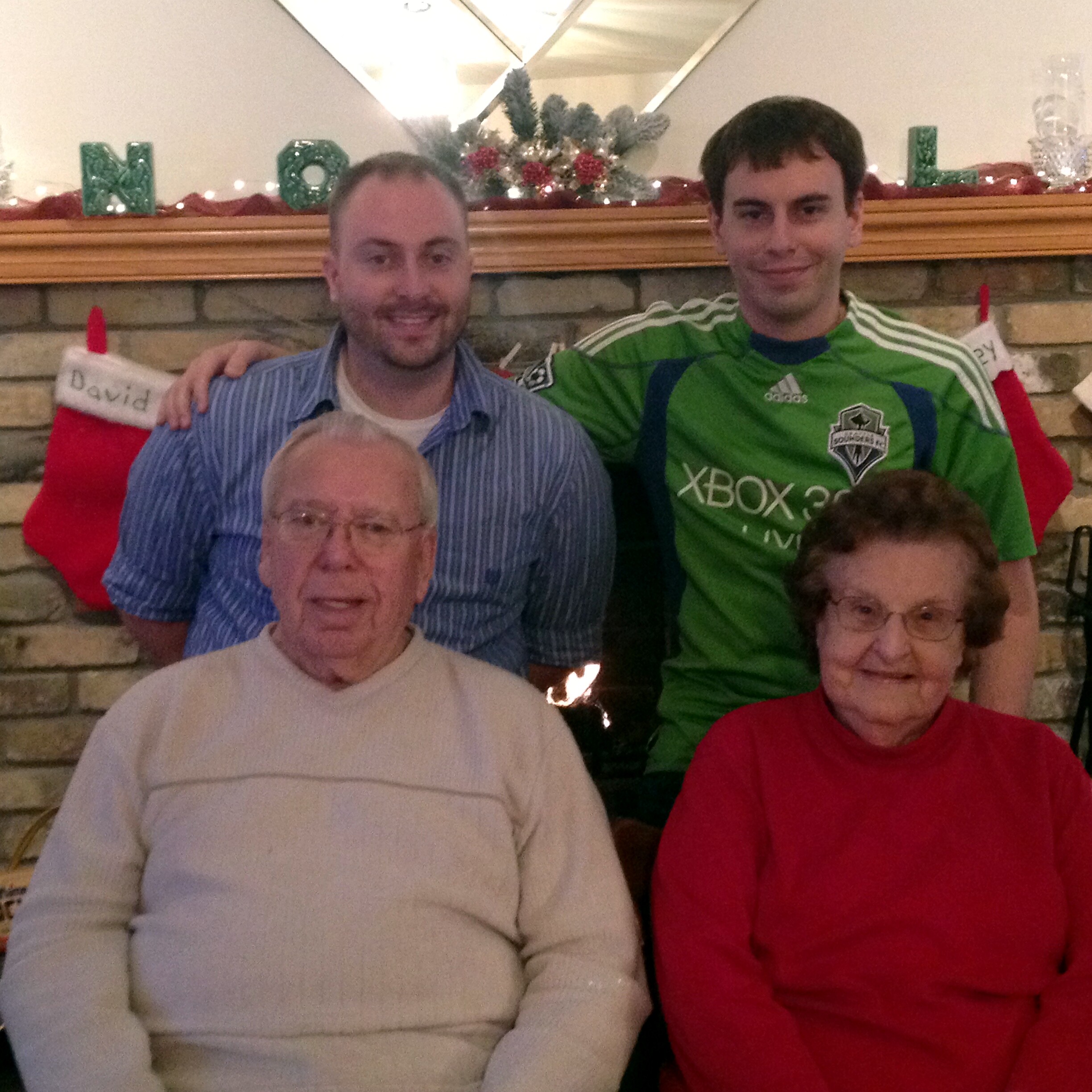 Group of people posing by a Christmas mantel with stockings and decorations, smiling at the camera.