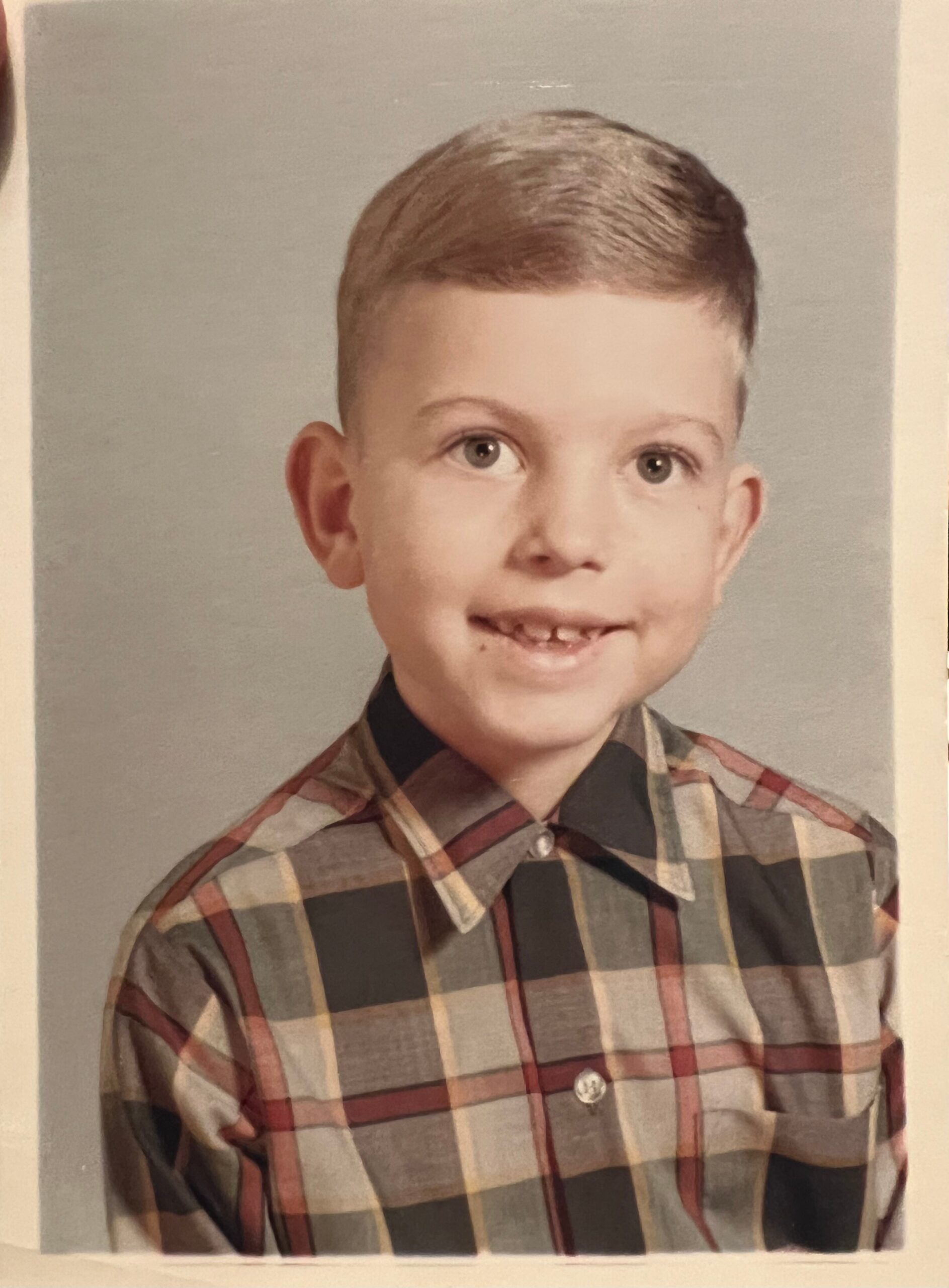 Smiling young boy in a plaid shirt posing for a school portrait.