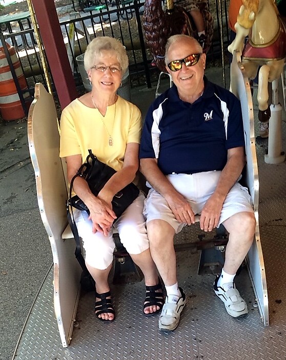 Older couple sitting side by side on a carousel ride seat, smiling as they wait for the ride to start.