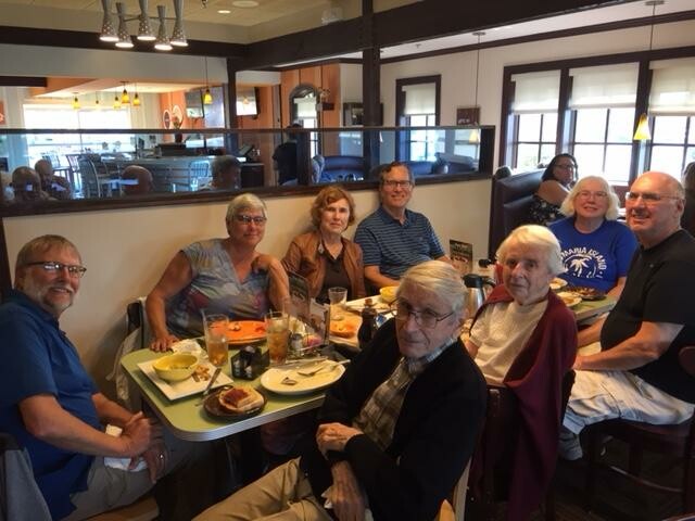 Group of nine seniors sitting around a restaurant table, enjoying meals together and posing for the photo.