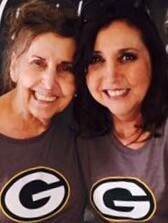 Two smiling women posing together in gray shirts with a circular black-and-yellow 'G' logo on the chest.