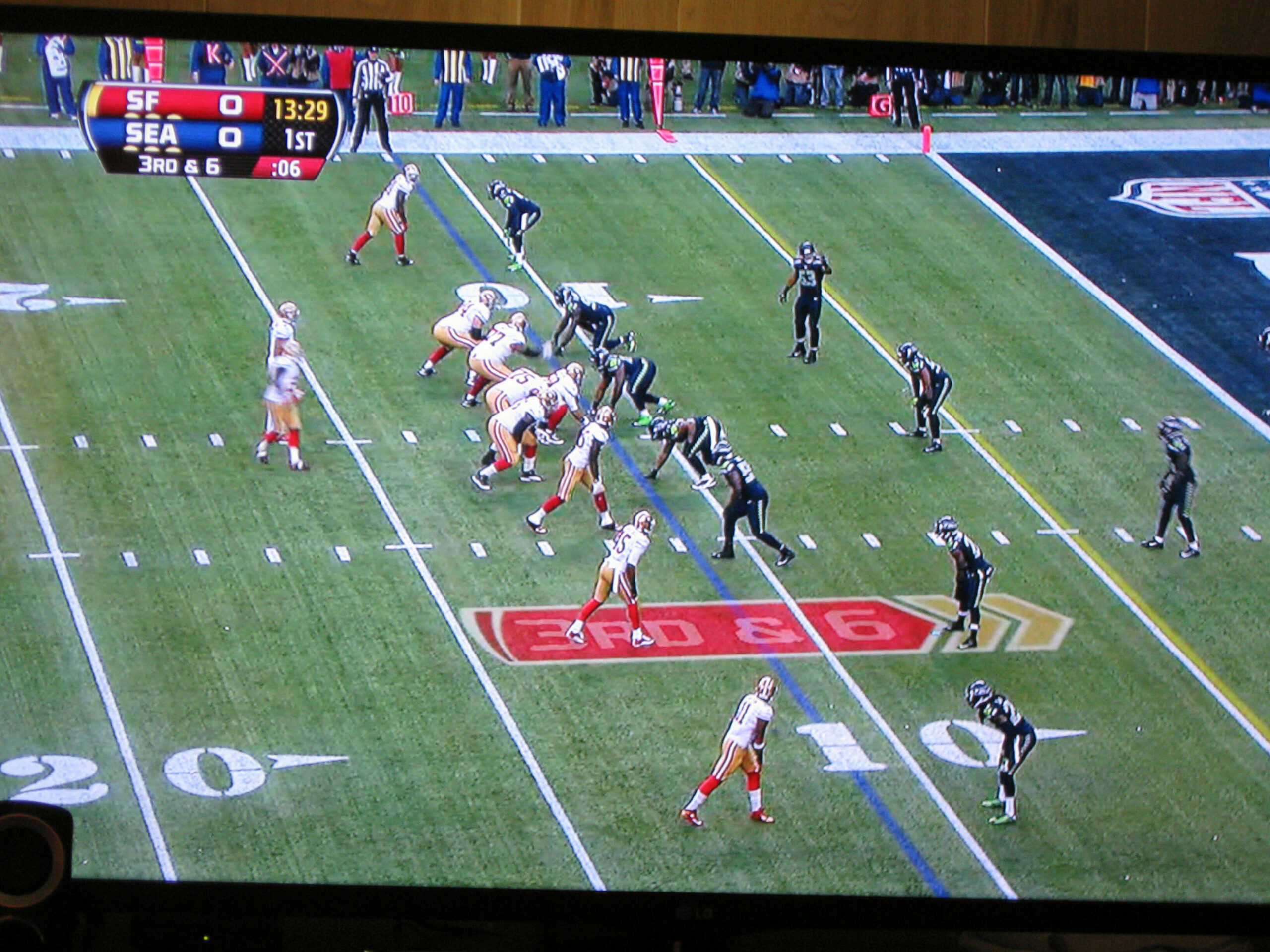 Football game: 49ers vs Seahawks, players line up at the scrimmage with a referee on the sideline; score 0-0, 13:29 left in 1st quarter.