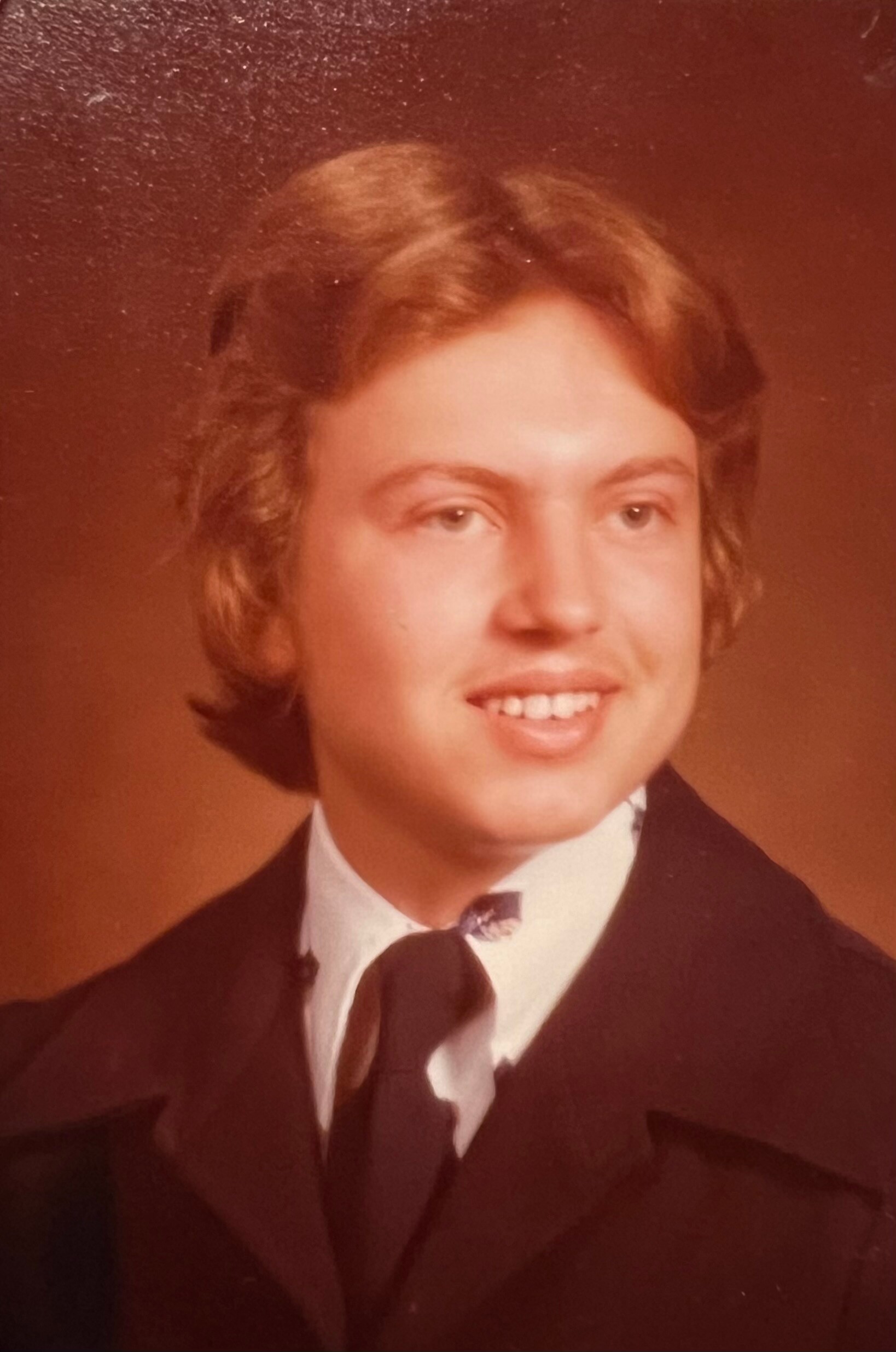 Young man in a black tuxedo, white shirt, bow tie, smiling for a studio portrait