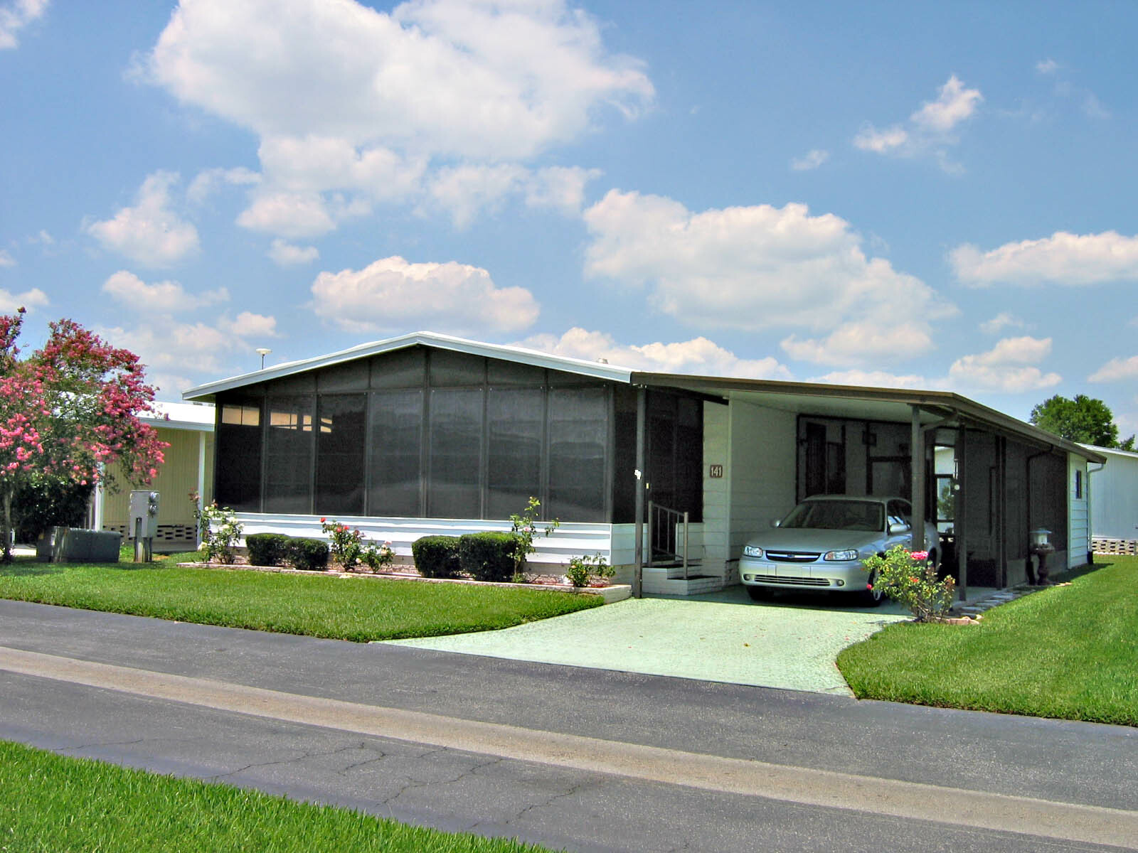 Single-story manufactured home with a screened front porch, carport, and a silver sedan in the driveway.