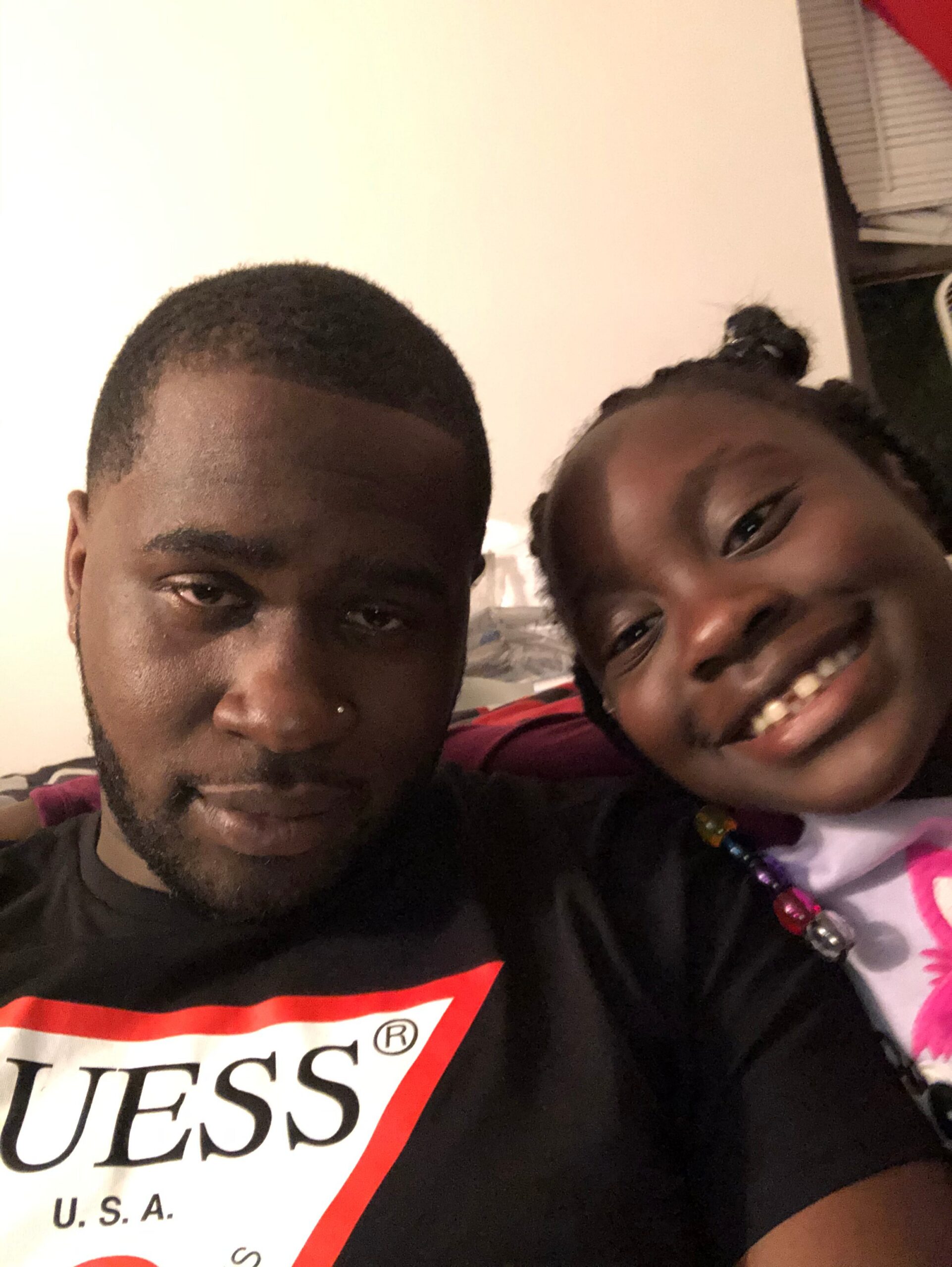 Close-up selfie of a man on the left and a smiling girl on the right; GUESS logo on their shirt.