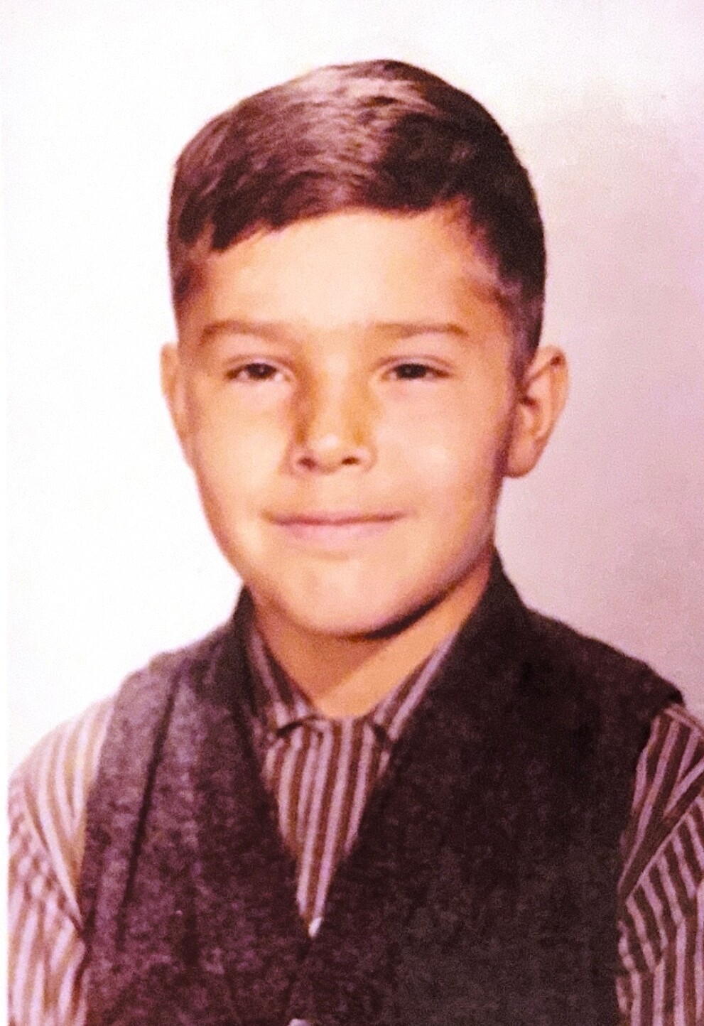 Young boy in a striped shirt and dark vest posing for a formal portrait photo.