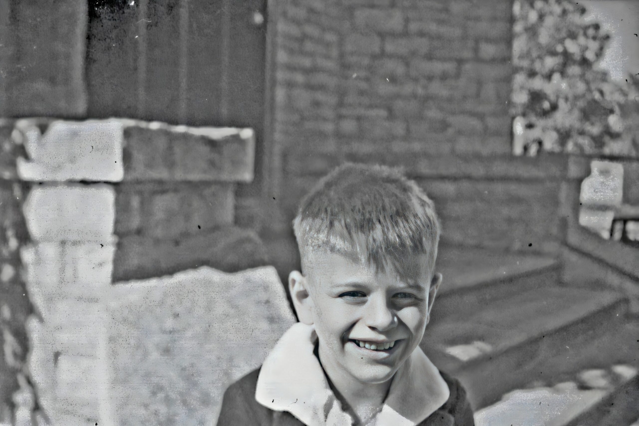 Smiling young boy outdoors in a coat, standing in front of a brick wall.