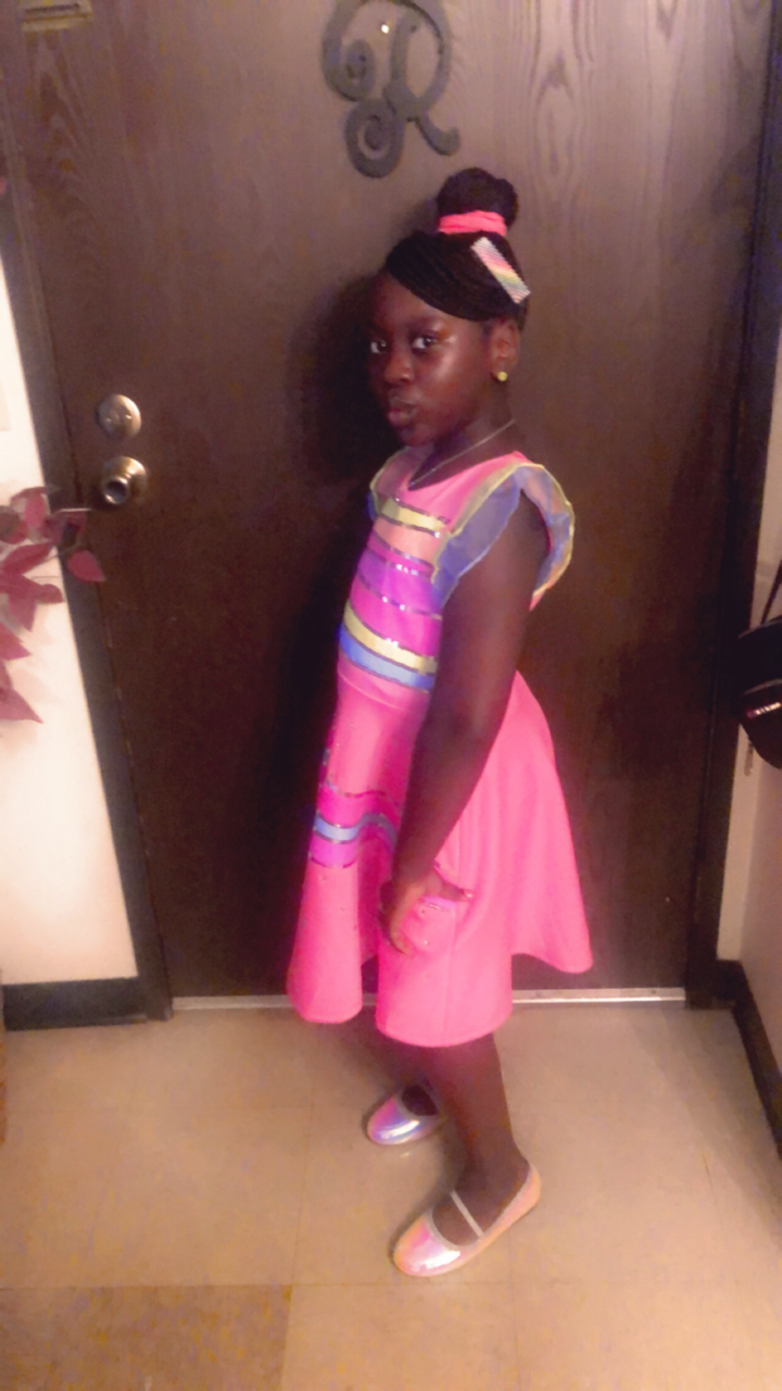 Girl in a bright pink striped dress posing sideways by a dark entry door indoors