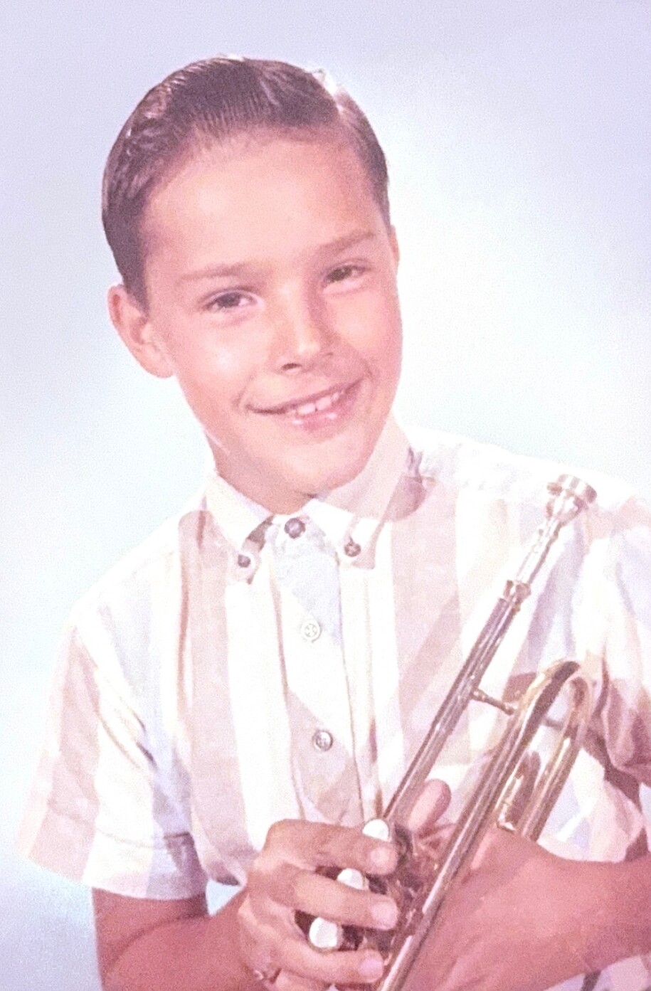 Smiling boy in a striped shirt holding a trumpet for a portrait.