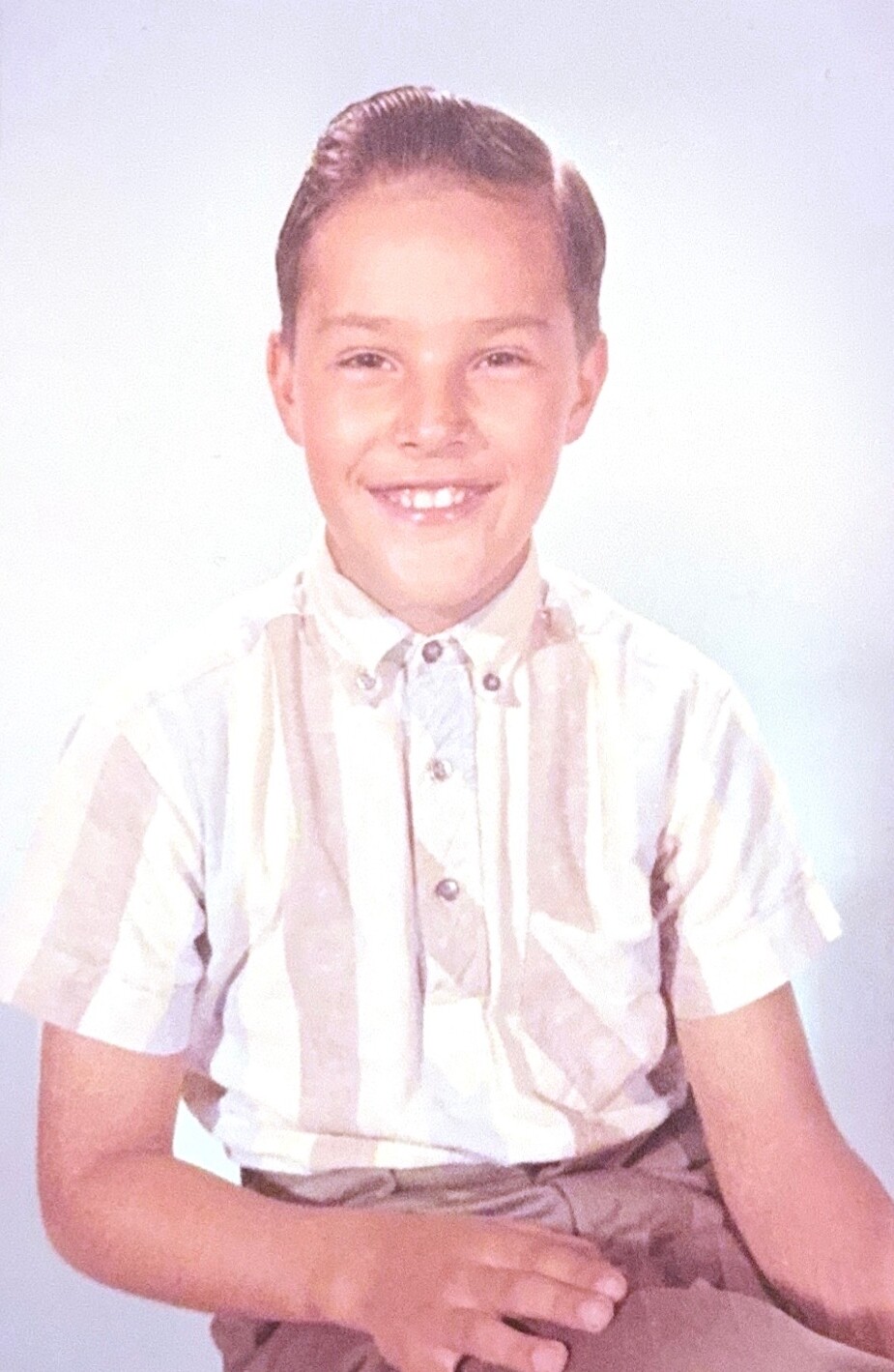 Smiling boy in a beige striped short-sleeve shirt poses for a studio portrait.