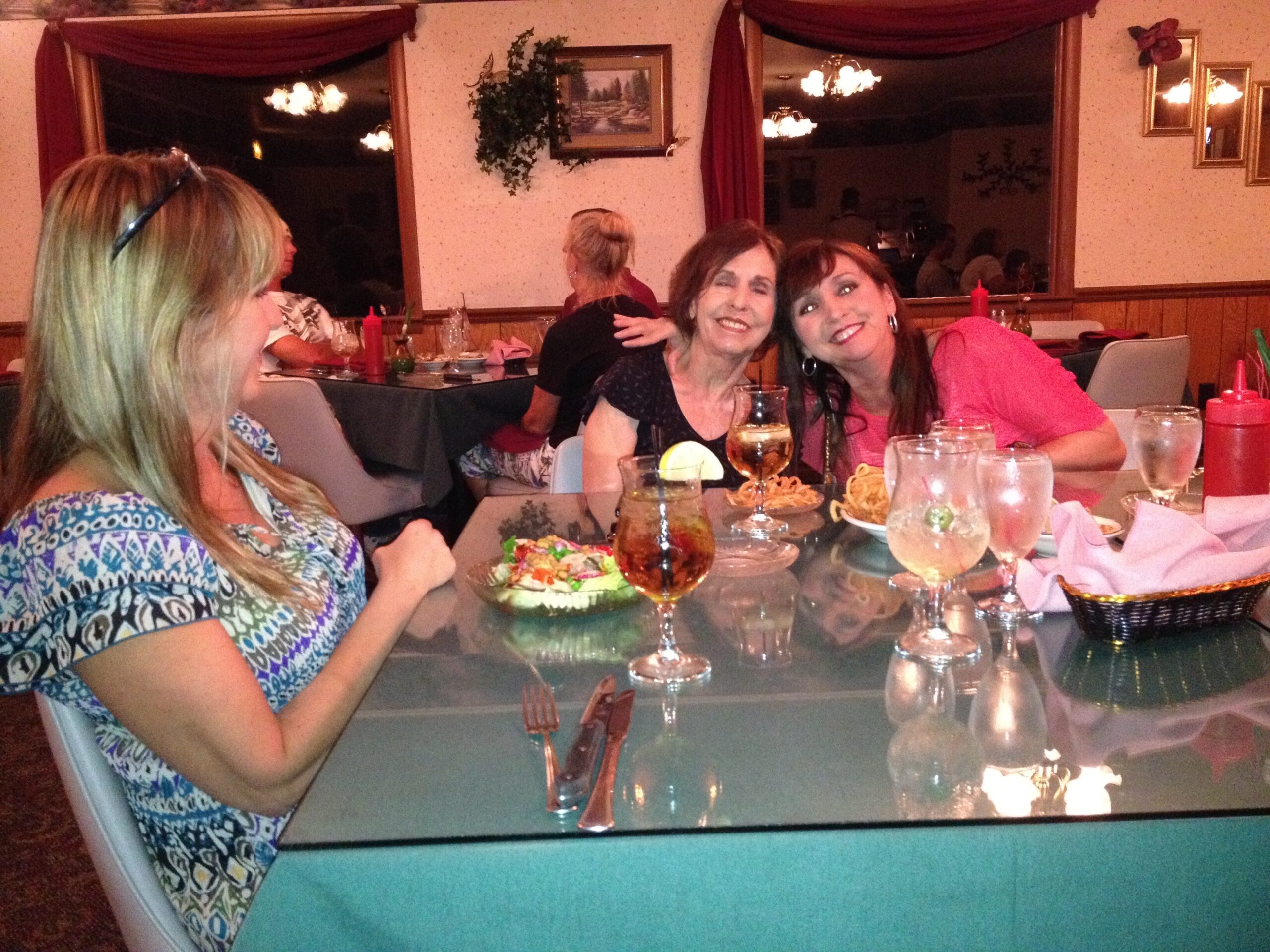Two women smiling at a dining table during a casual dinner, with drinks and snacks in front.