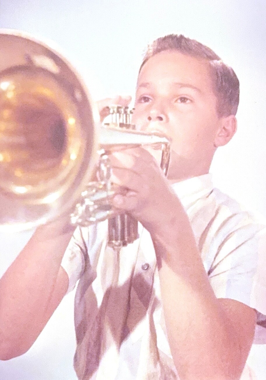 Young boy blowing into a brass trumpet, focused on playing music in a studio shot.