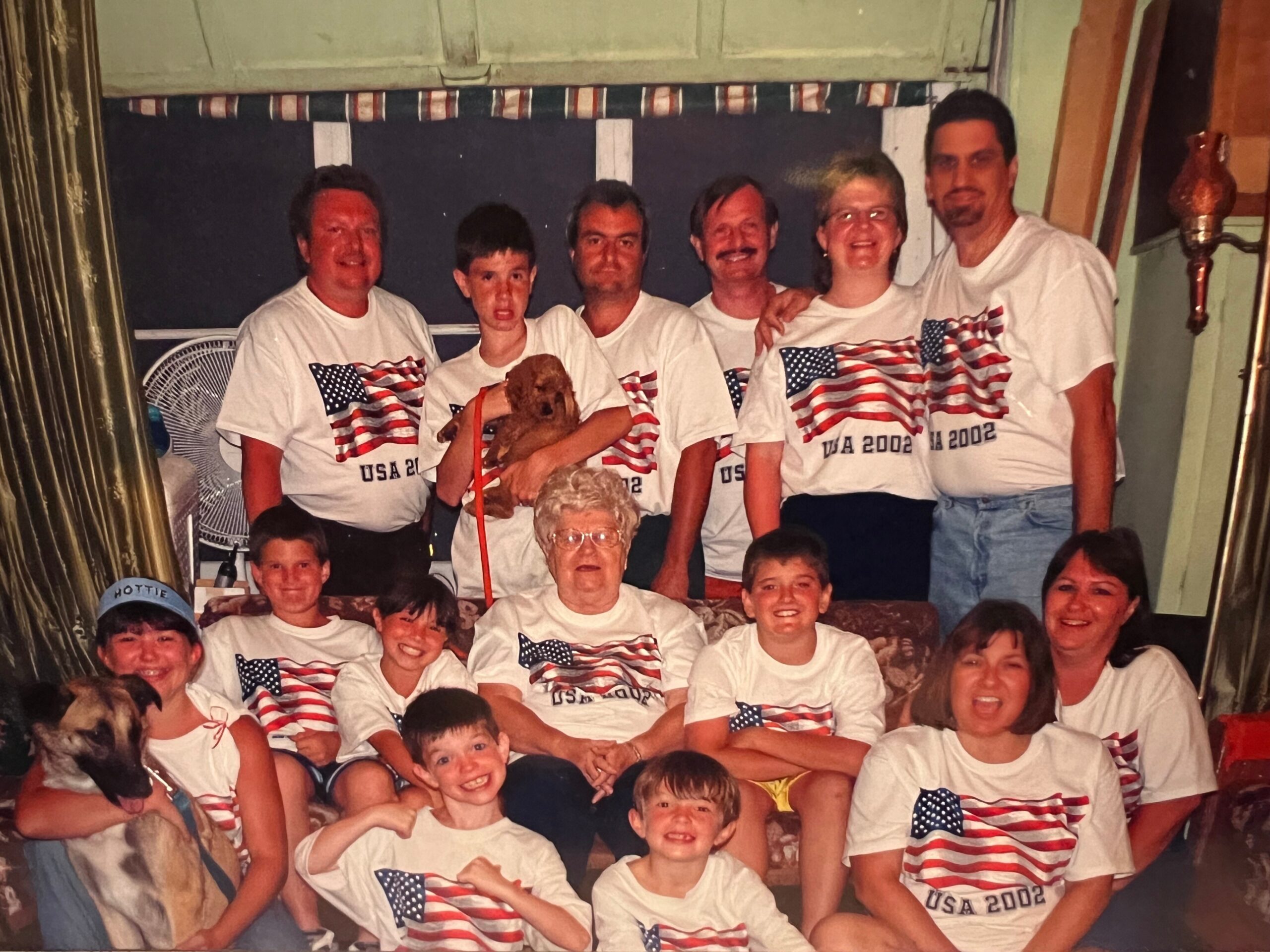 Group of people wearing matching USA 2002 shirts posing together in a room, with a dog visible in the front left.