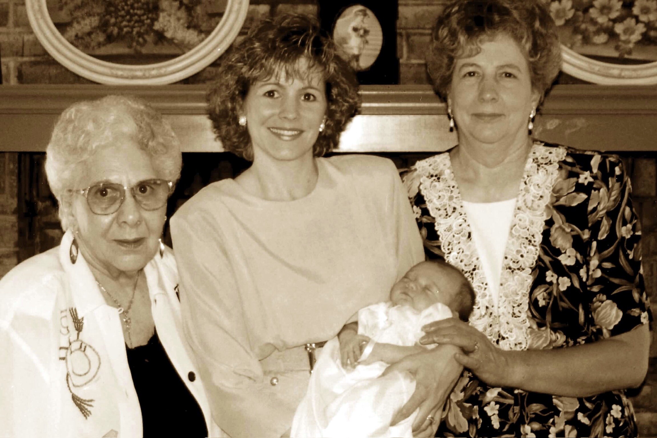 Three generations posing together with a newborn baby in a living room; woman in center cradles the baby as two older women smile nearby (sepia-toned).