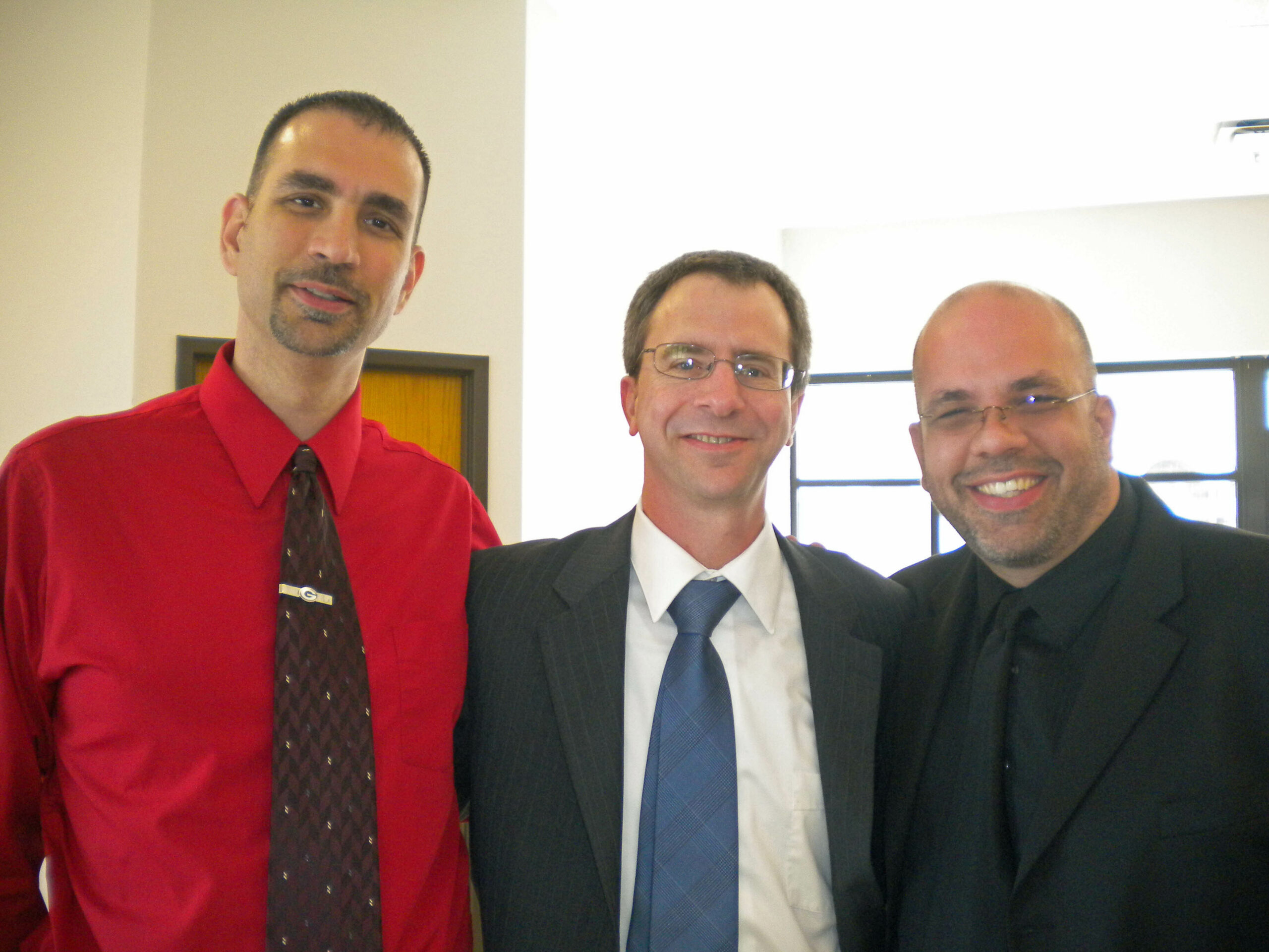 Three men in business attire posing for a photo indoors, smiling at the camera.