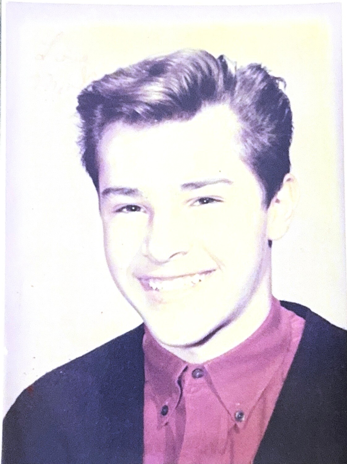 Smiling young man with dark hair wearing a burgundy shirt and dark blazer, posing for a portrait.