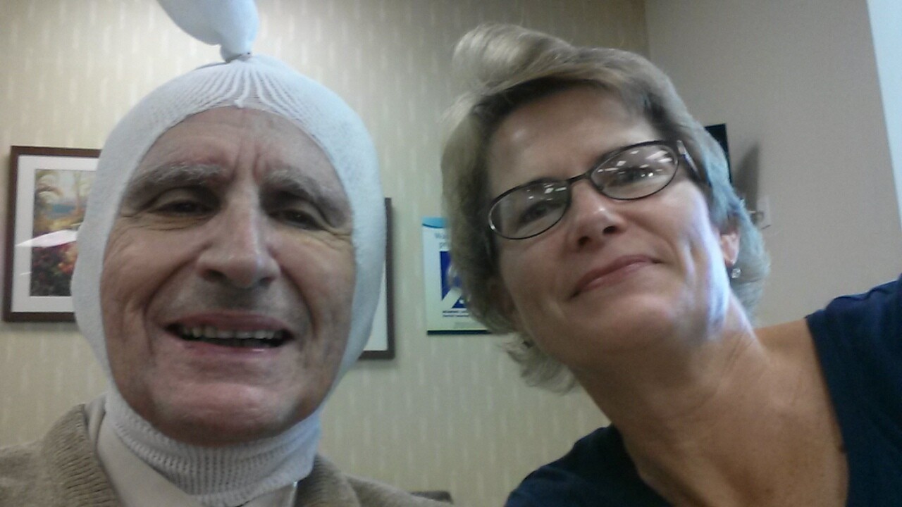 Two women posing for a selfie; man on the left wears a white head wrap, smiling, while a woman with glasses sits to his right.