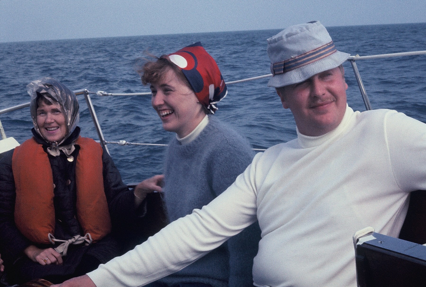 Three adults on a boat at sea, smiling and wearing life jackets; blue ocean in the background.