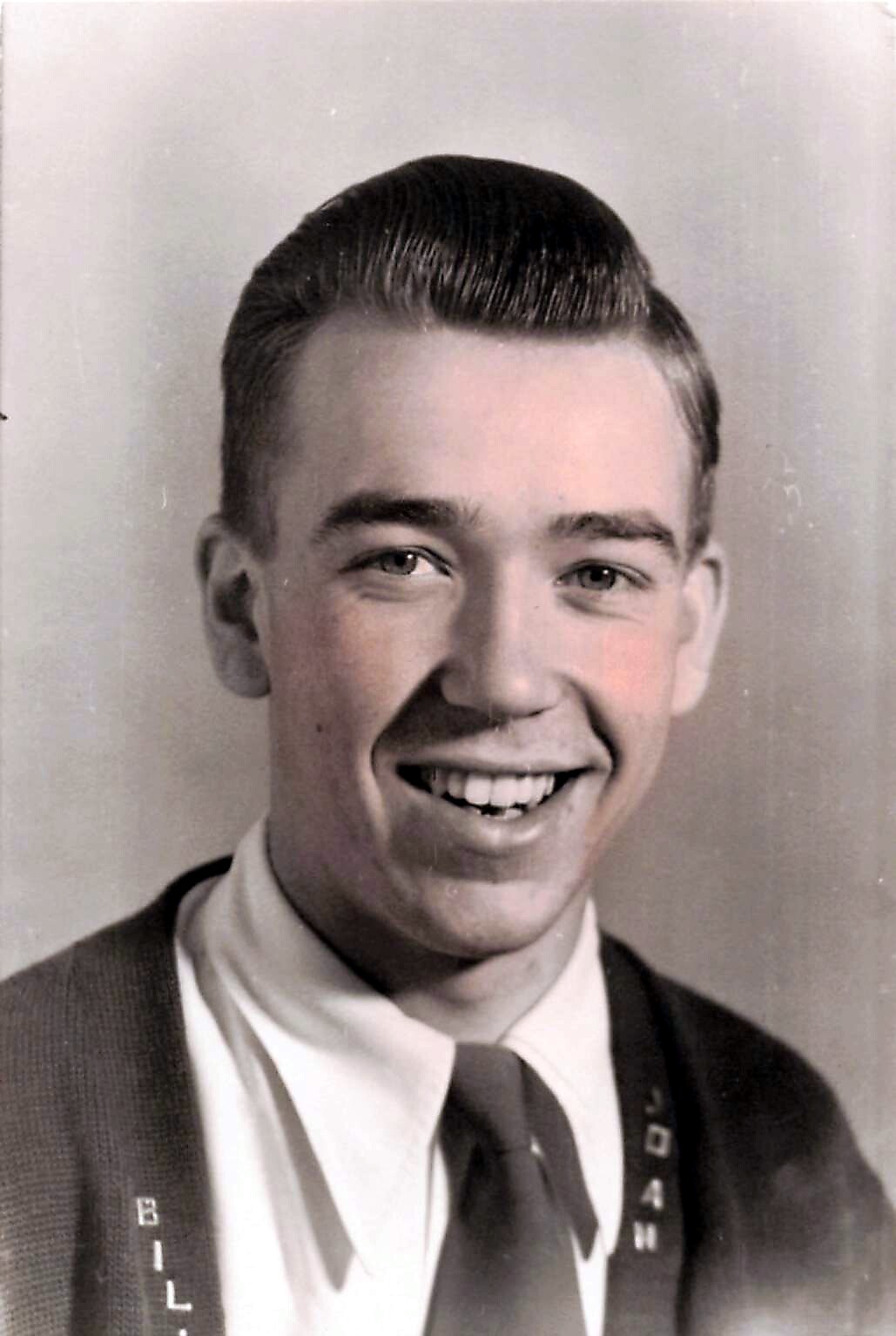 Smiling young man in a suit and tie, studio portrait, black-and-white photo with slicked-back hair.