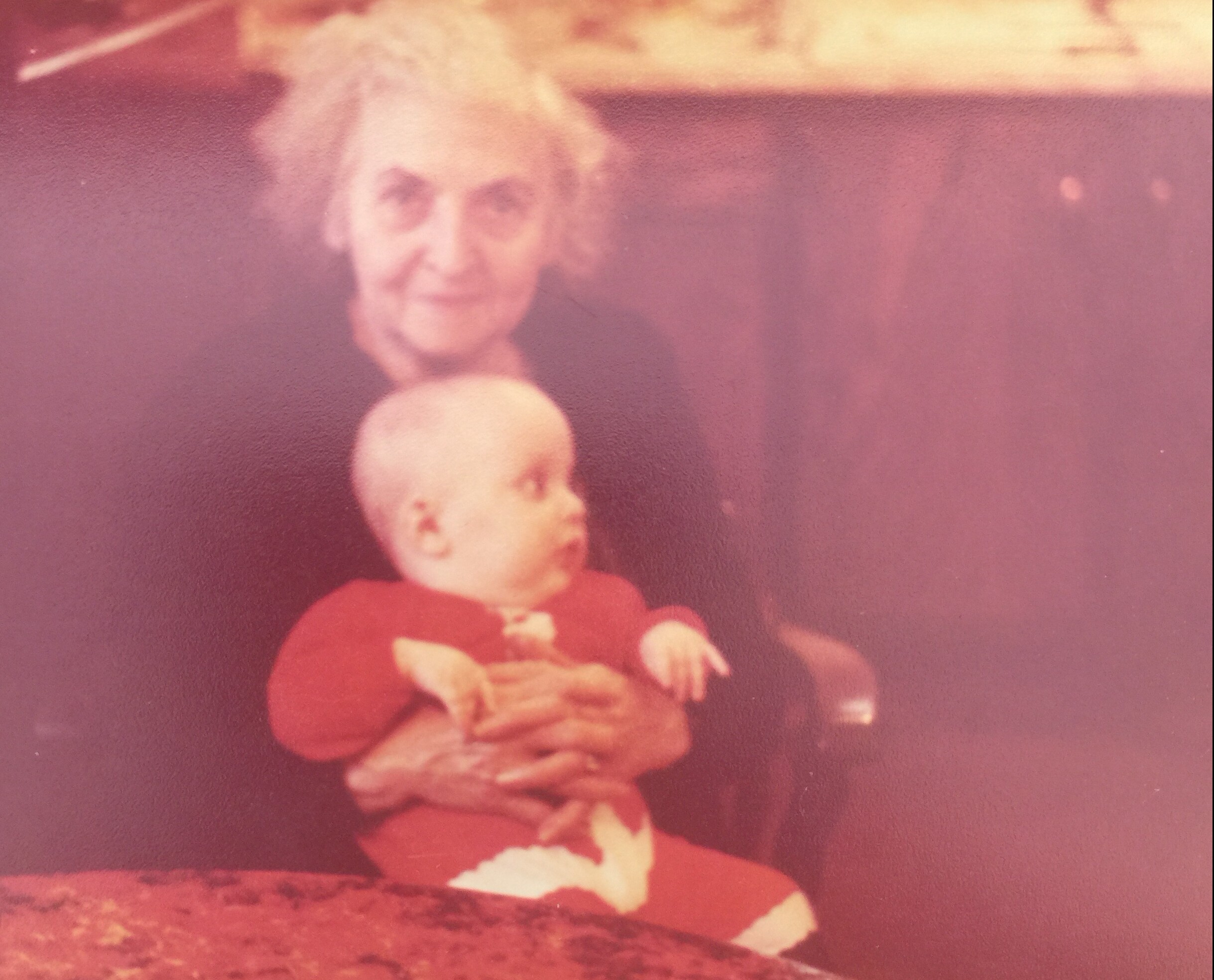 Blurry vintage photo of a young child in a red dress with white patterns, standing with hands clasped in front.