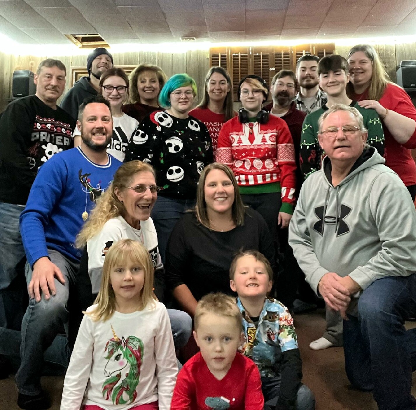 A group of people wearing festive Christmas sweaters posing together indoors, smiling for the photo.