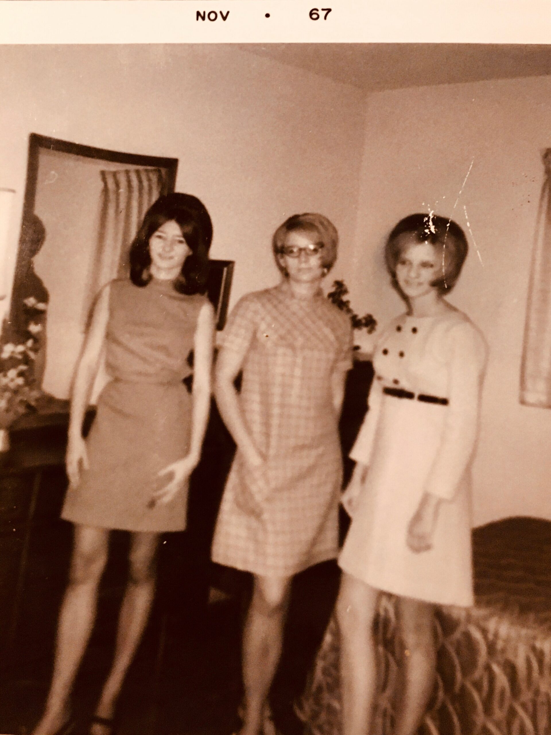 Three women pose together in a living room, wearing 1960s dresses; date marked Nov 67.