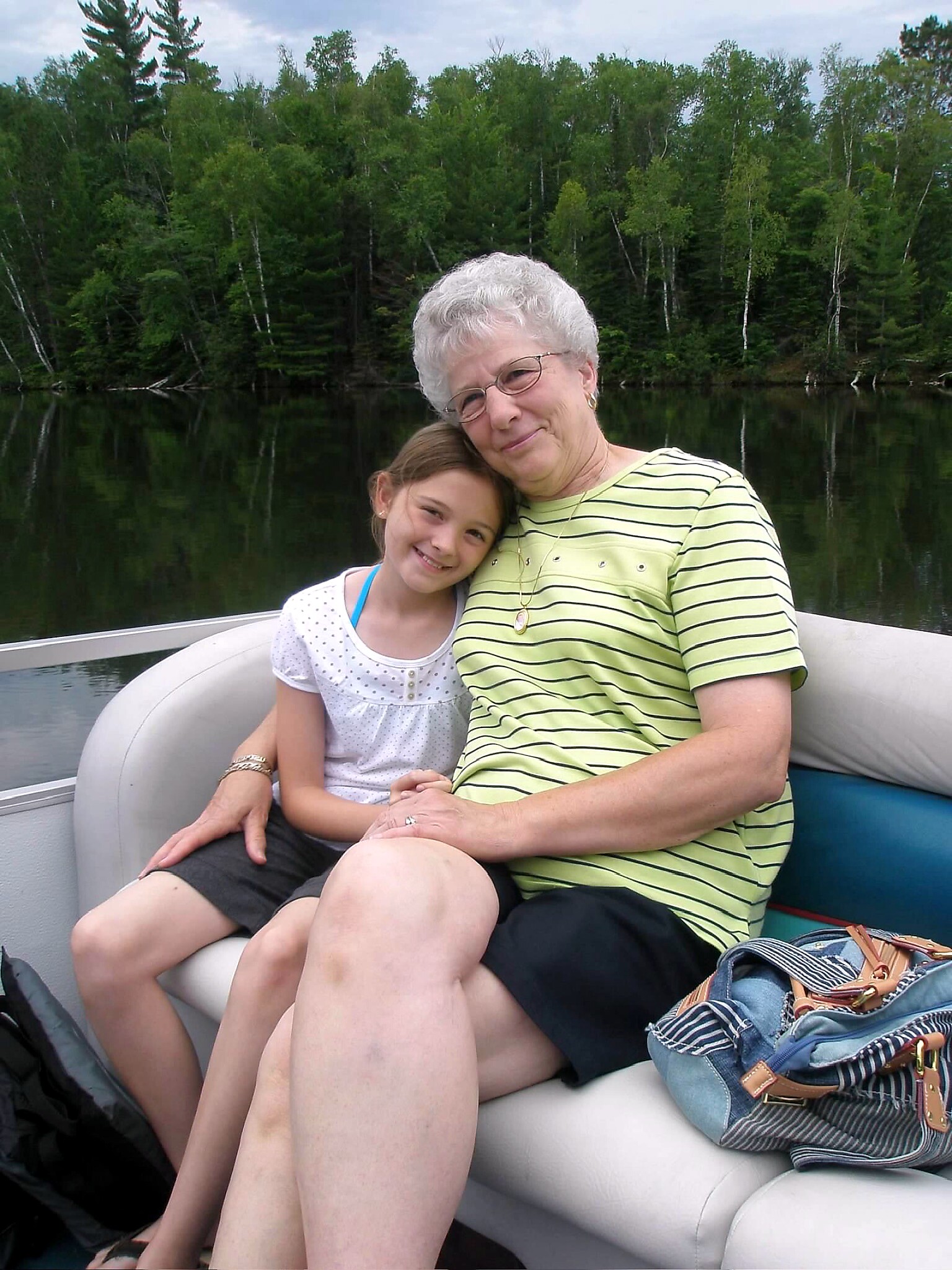 Grandmother and granddaughter smiling together on a boat, with a forested lake in the background.