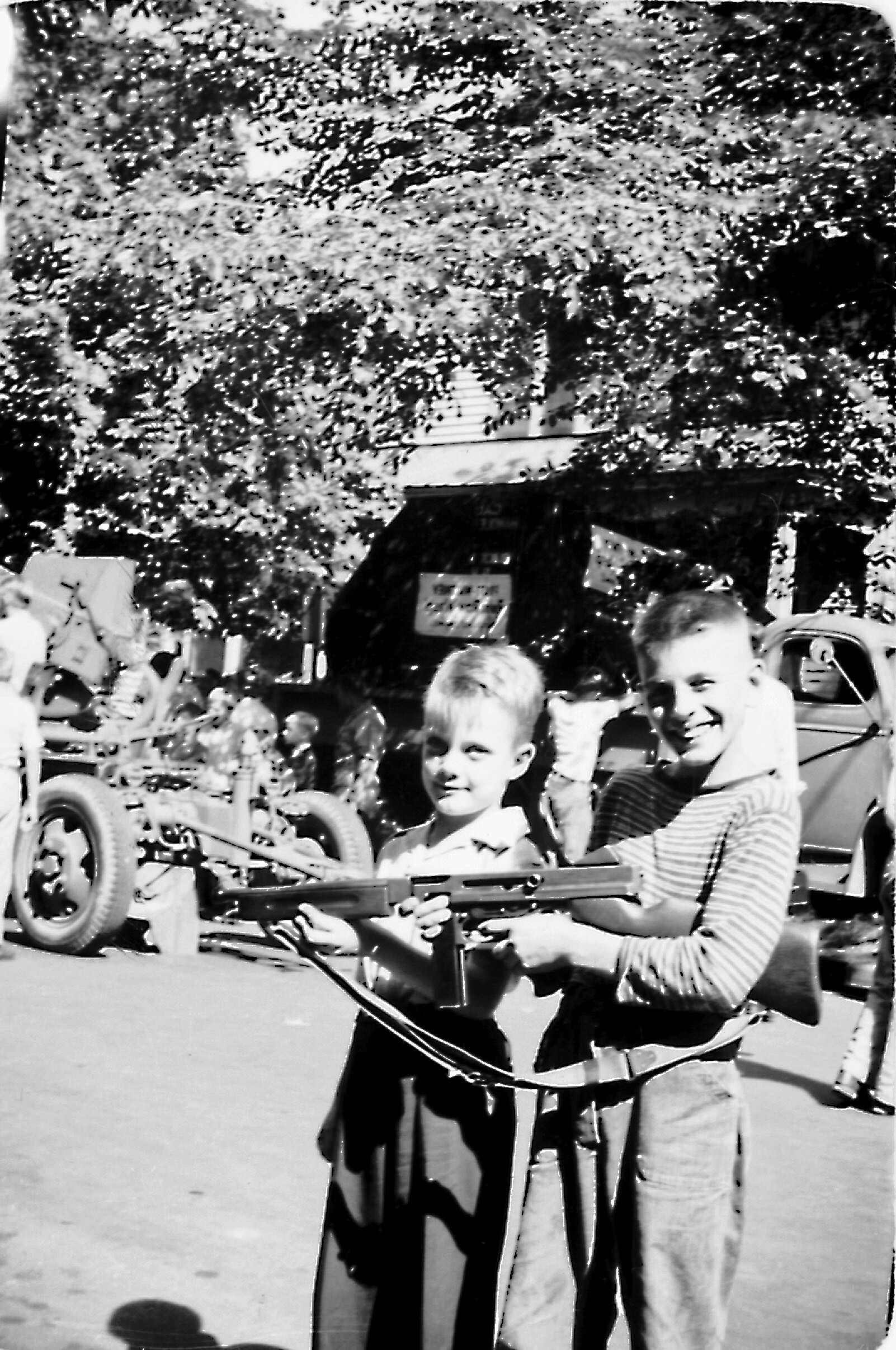Two smiling boys in striped shirts stand in front of a crowd at a street parade, with bicycles visible behind them.