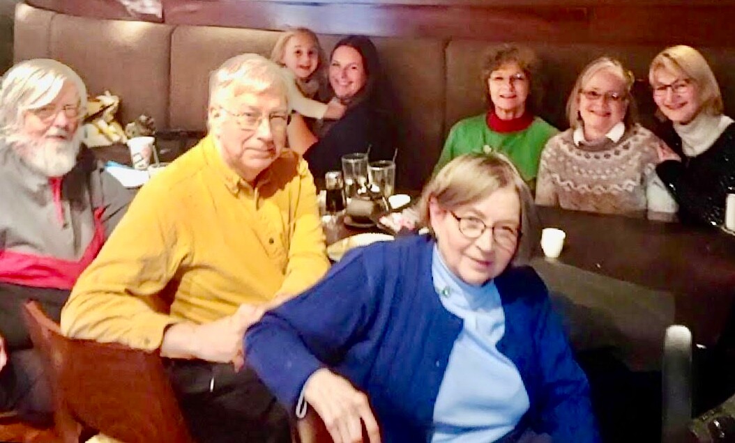 Group of people gathered around a restaurant table posing for a photo, smiling at the camera.
