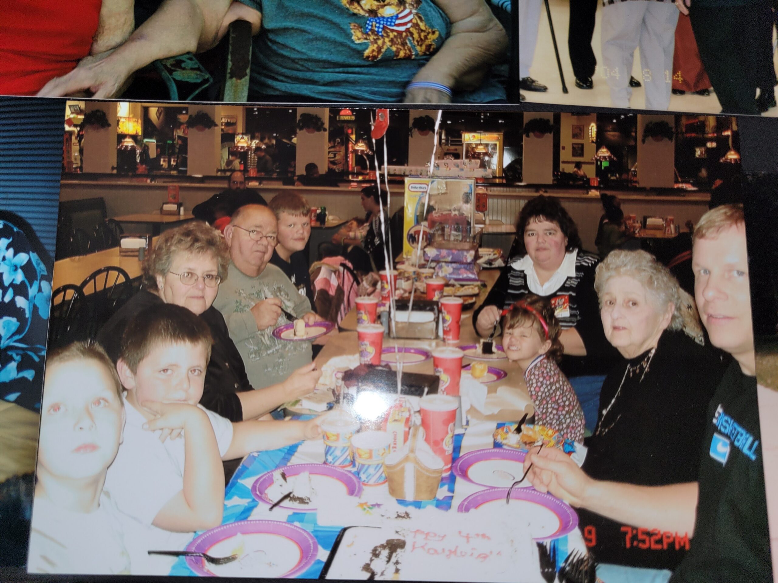 Group of family members seated at a long restaurant table, enjoying cake and drinks during a celebration.