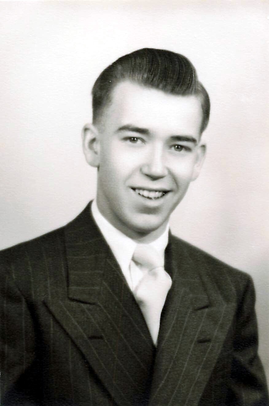 Young man in a pinstripe suit and light tie, smiling for a formal portrait in black and white.