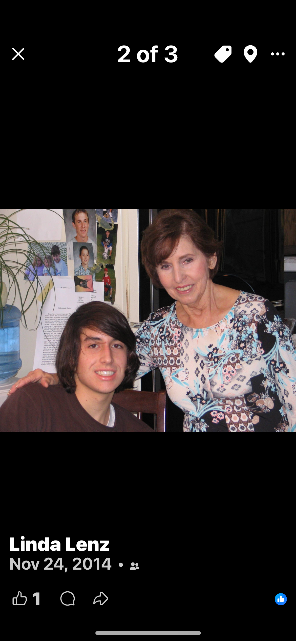Two people pose together indoors: a young man with dark hair seated beside an older woman with short brown hair, both smiling.