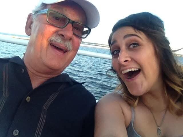 Two people on a boat taking a selfie, smiling with open water in the background.