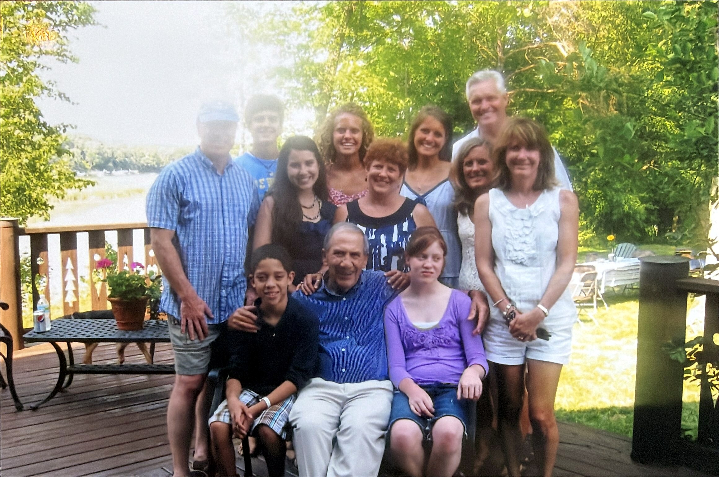Group of adults and children posing for a photo on a wooden deck with a lake and trees in the background.