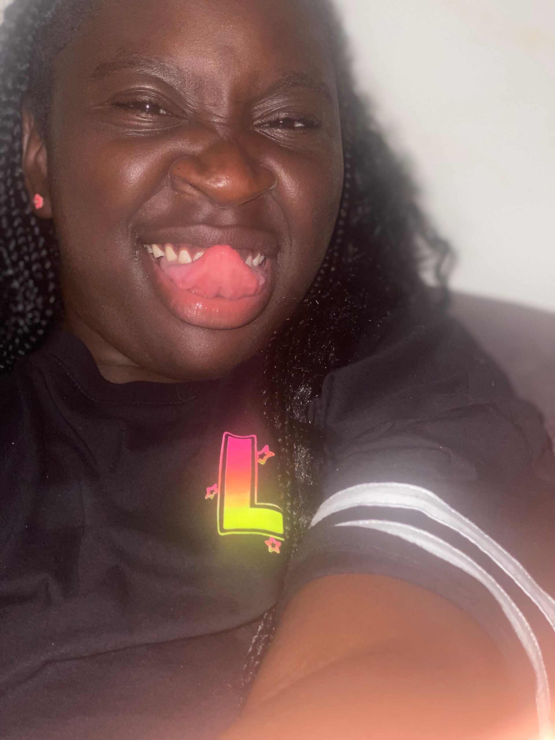 Close-up selfie of a smiling girl sticking out her tongue playfully, wearing a black shirt and pink earrings.