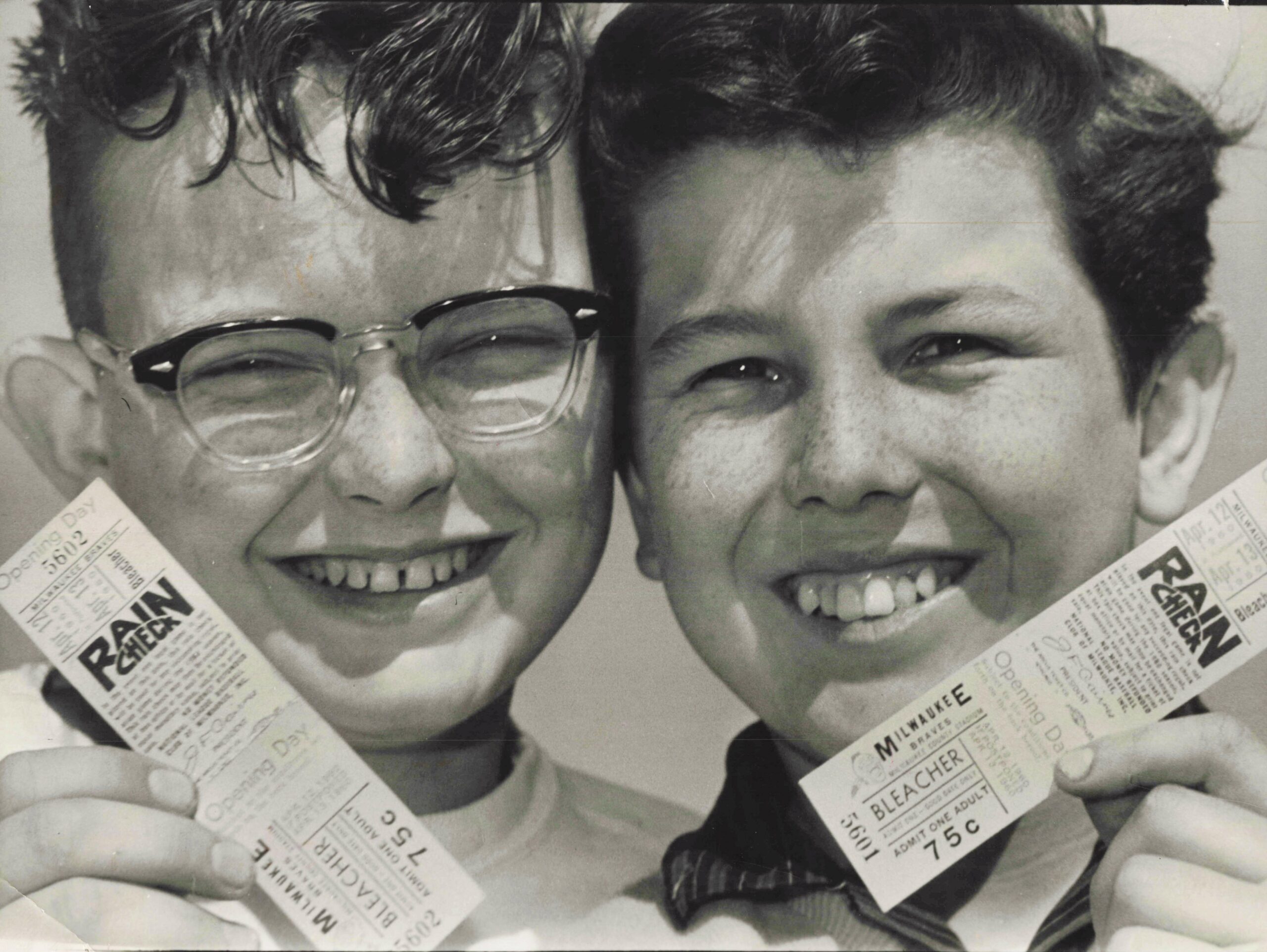Two friends smiling for a close-up photo, each showing vintage Milwaukee Braves tickets in the frame.