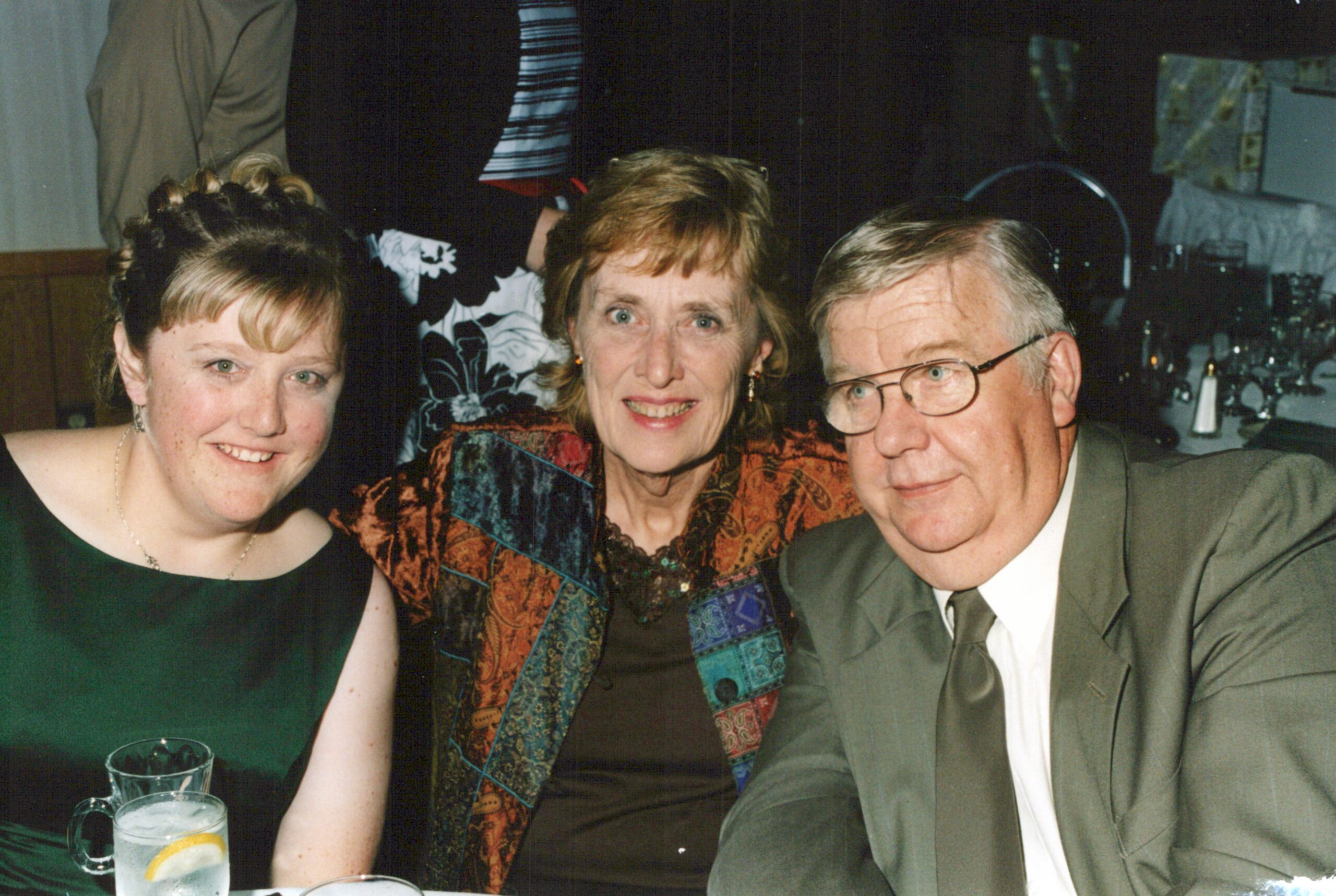 Three adults posing at a dinner: woman in green on the left, woman in a patterned jacket in the center, man in a gray suit on the right.
