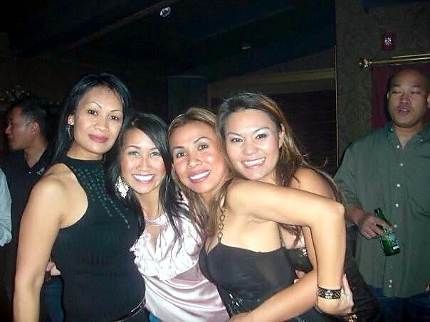 Four smiling women posing together in a dim nightclub, arms around each other, enjoying a night out.