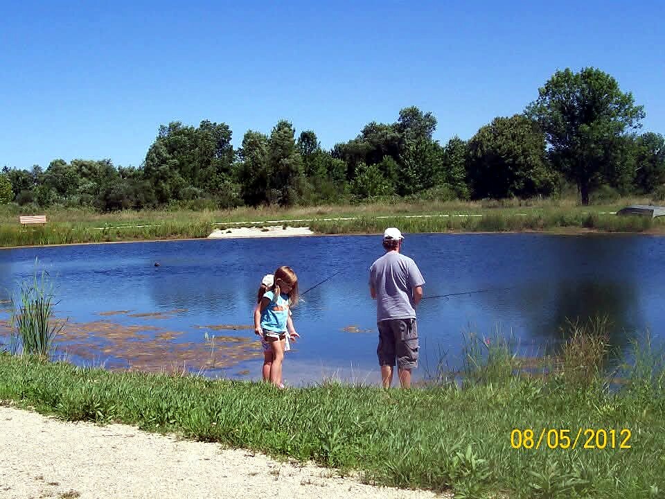 Man and girl fishing at the edge of a blue pond on a sunny day; date stamp 08/05/2012 in the corner.