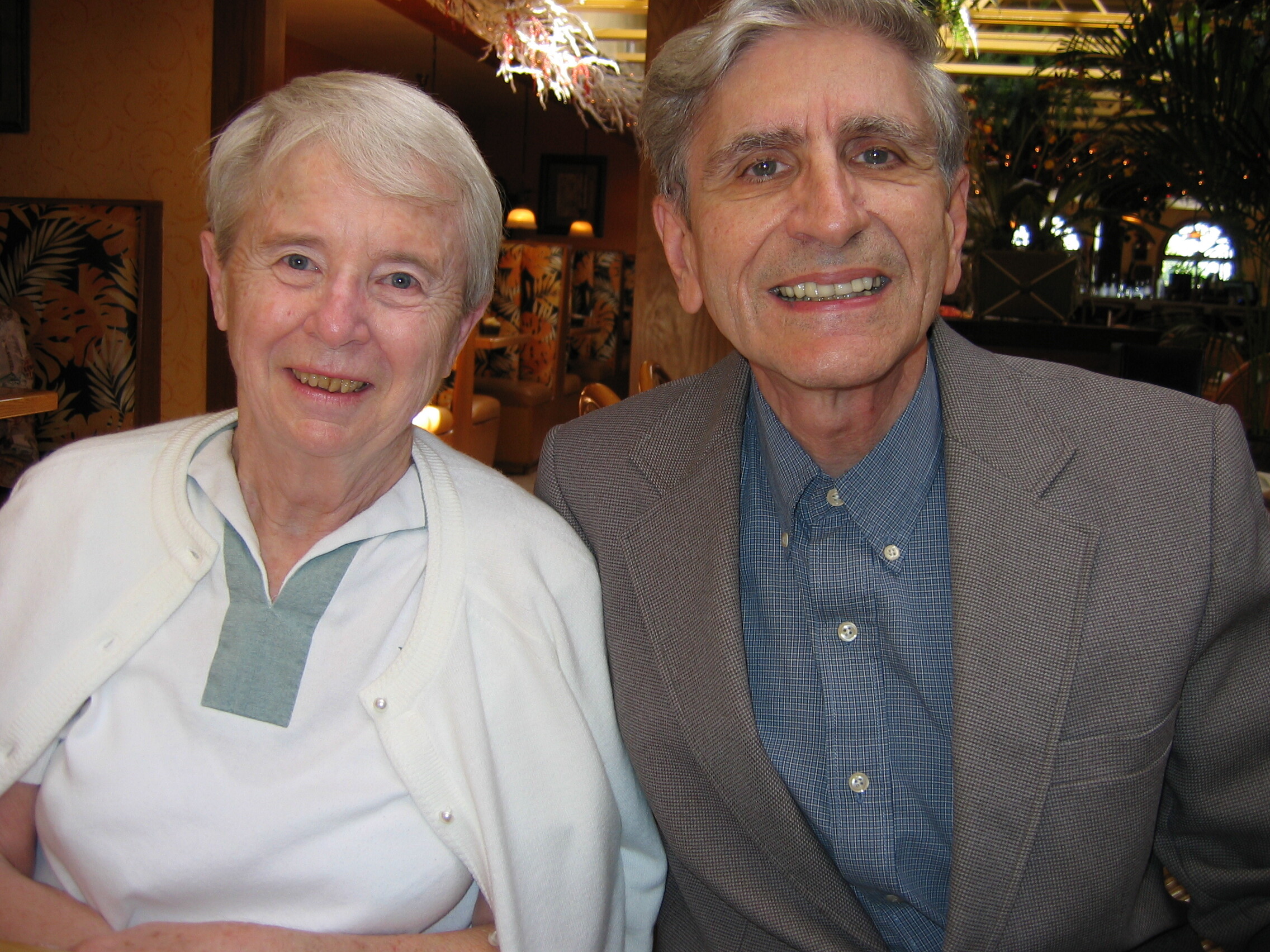 Smiling elderly couple posing for a photo in a restaurant or cafe setting.