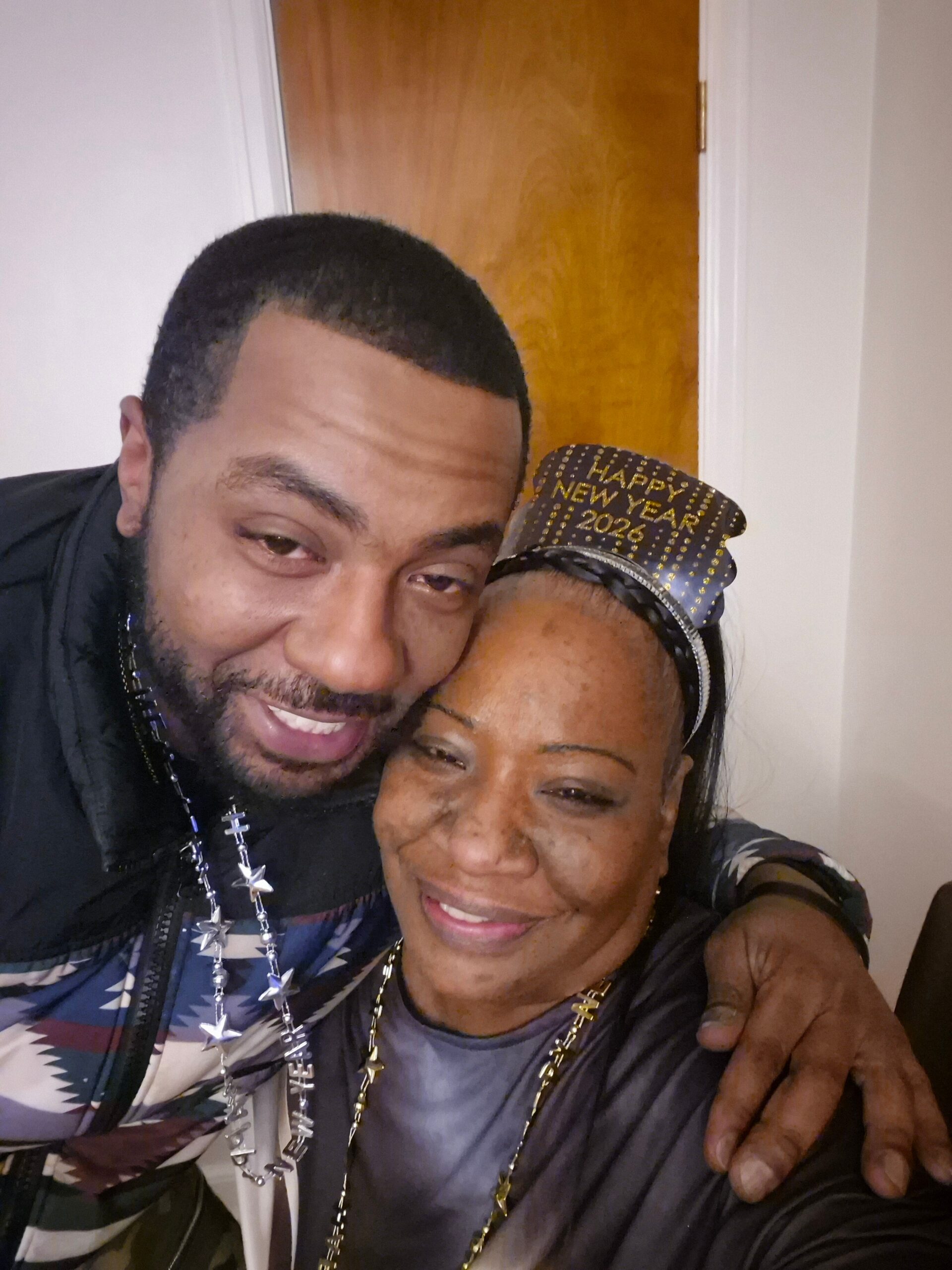 Close-up selfie of two people smiling, with the woman wearing a festive hat that says 'Happy New Year 2024'