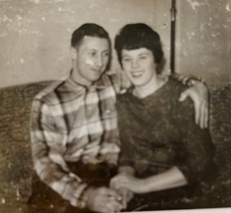 Vintage photo of a couple cuddled close on a sofa, smiling at the camera.