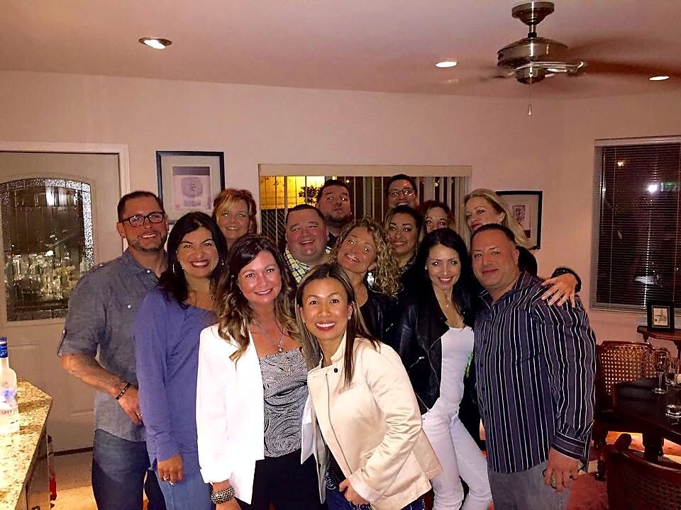 Group of about fifteen adults posing together for a photo in a home living room.