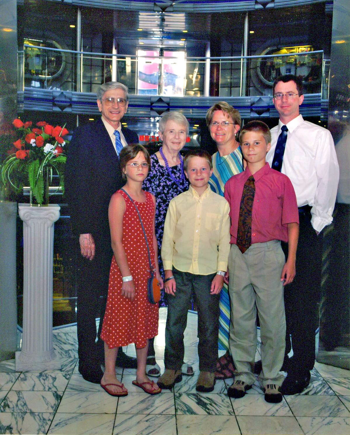 Family portrait of seven people in a hotel lobby, posing together in formal attire beside a flower arrangement and marble floor.