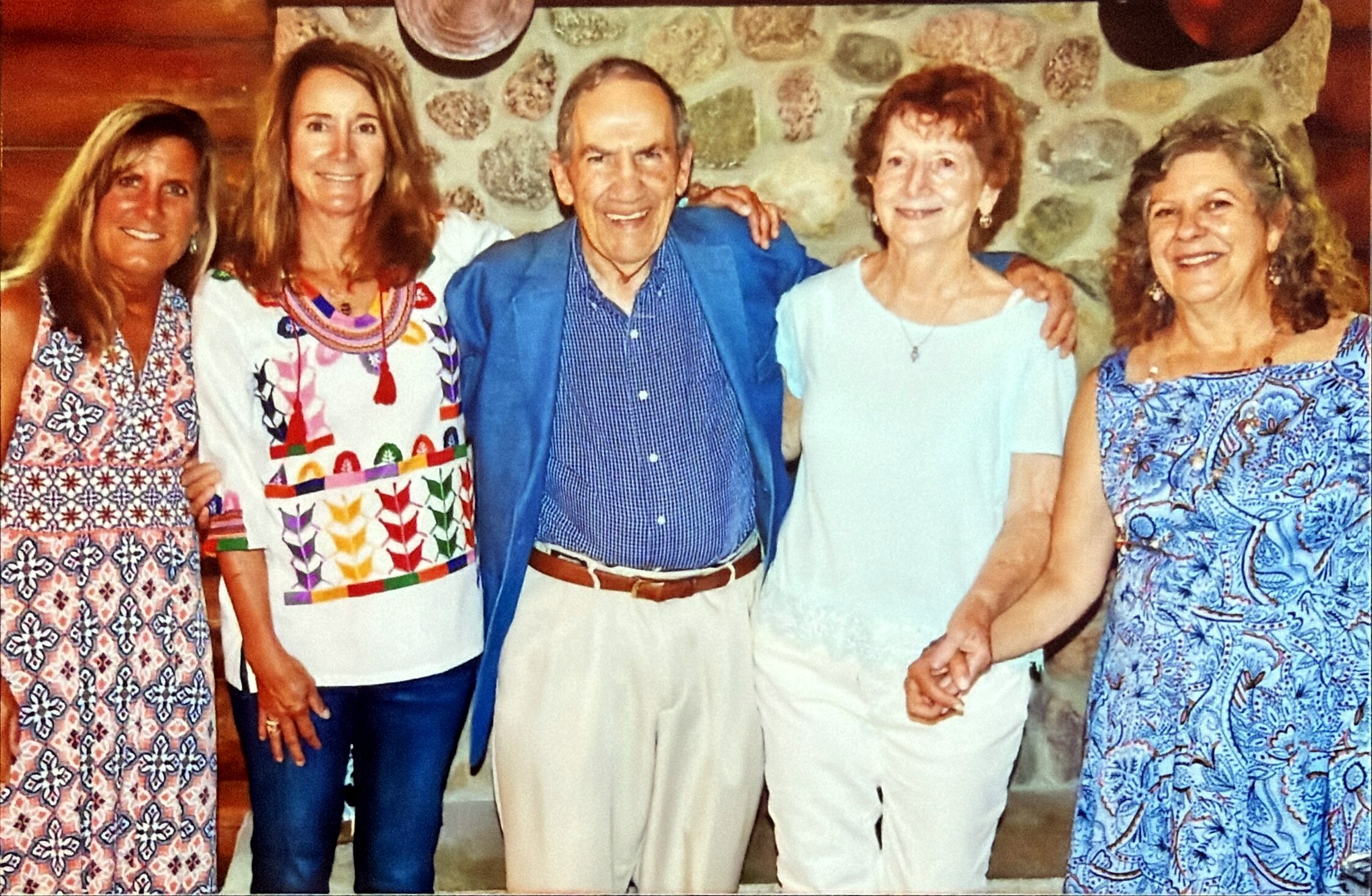 Six adults posing together with arms around each other, smiling at the camera against a stone wall backdrop.